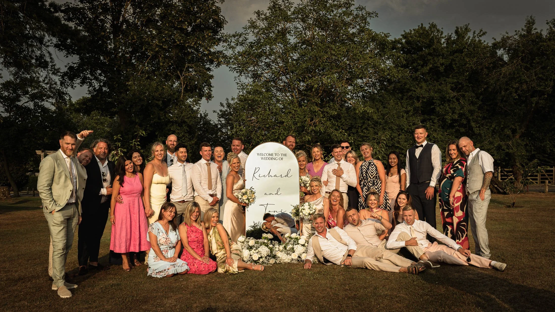 A bride and groom dip and kiss in the reflection of a mirror that is surrounded by their bridal party and closest friends in an artistic wedding photograph captured at Winters Barns in kent.