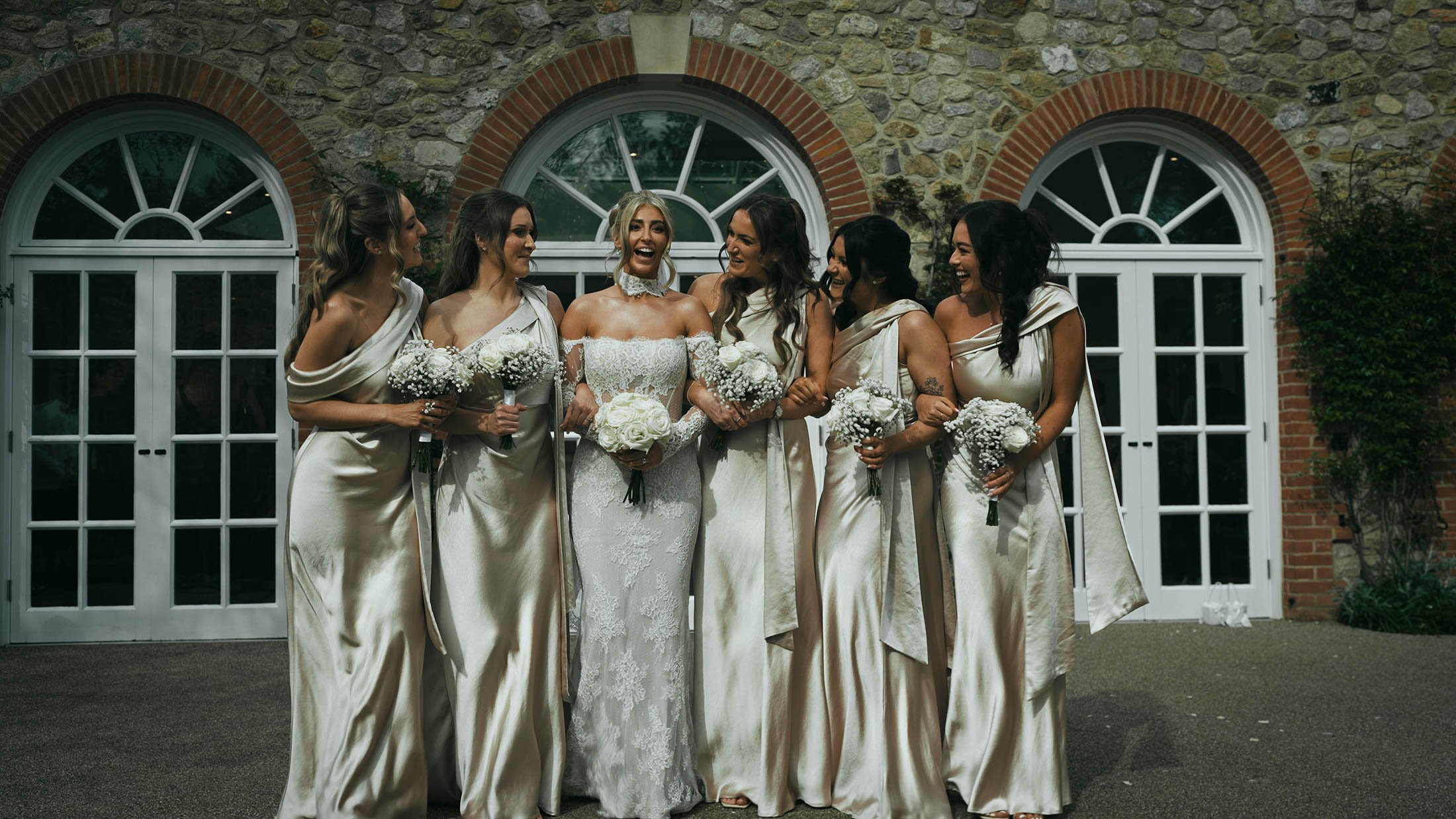 A bride and her bridesmaids walking together outside the Orangery in Maidstone, as part of a storytelling wedding film in the UK.