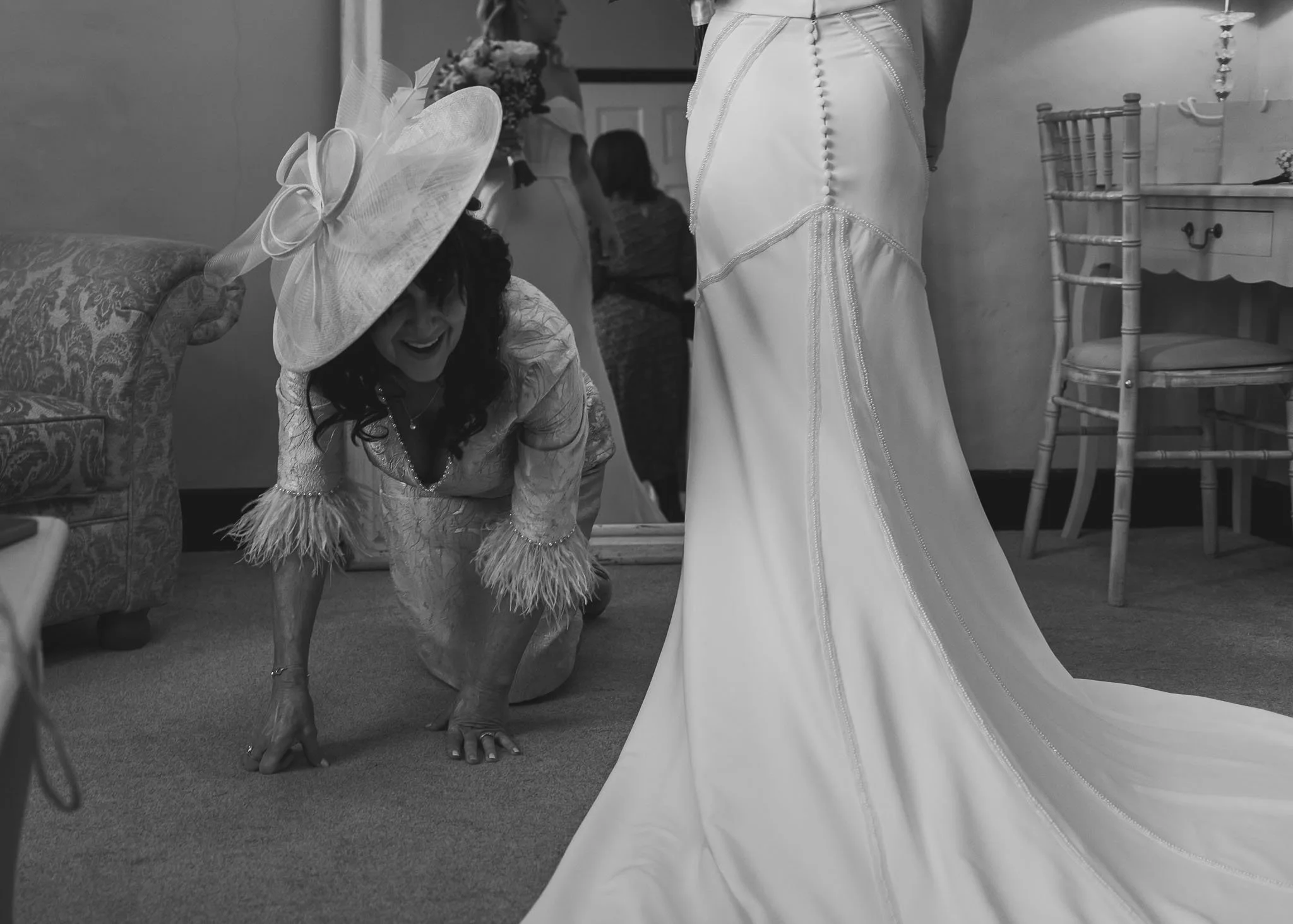 Candid moment of the mother of the bride crawling on the floor to fix the brides dress, framed in an editorial style.