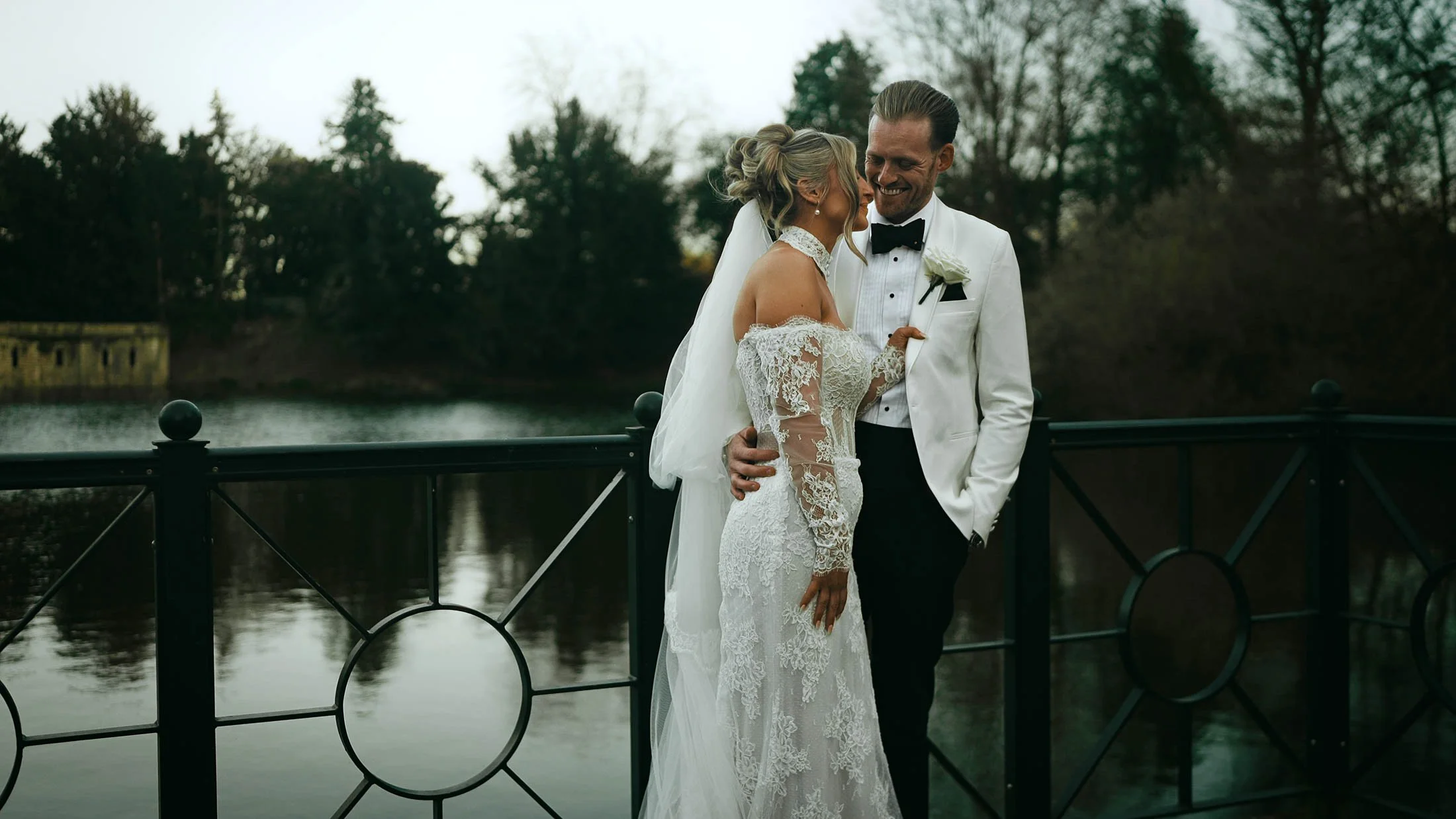A bride and groom smile at each other by the lake at the Orangery, Maidstone.