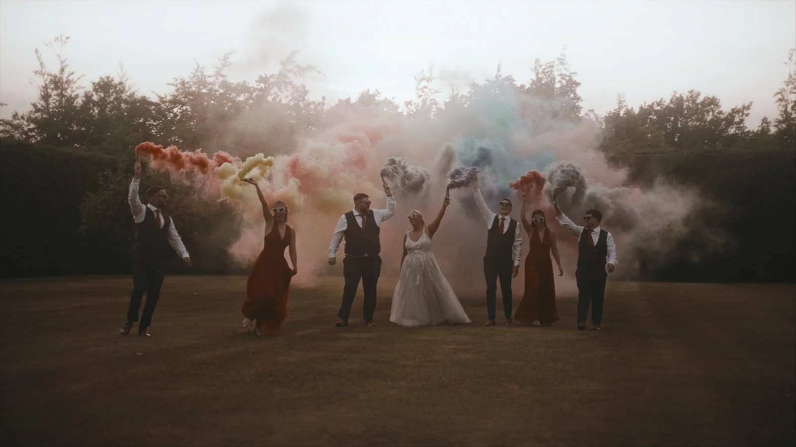 A bridal party walk through the grounds of Winters Barns wedding venue holding brightly coloured smoke bombs in a cinematic wedding film.