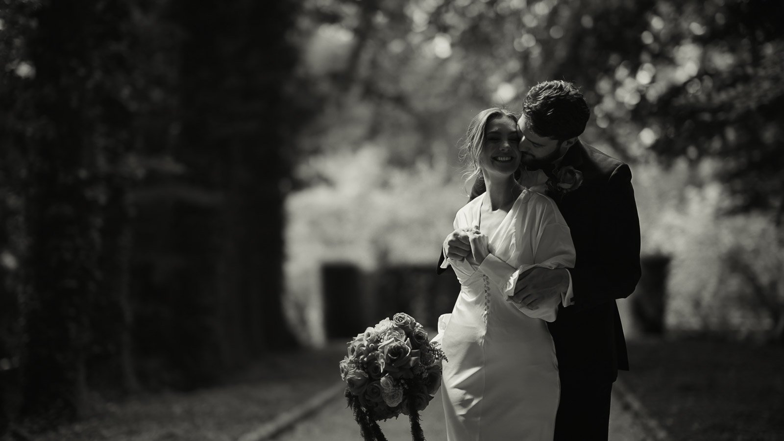 Timeless couple moment during a black tie wedding as the couple laugh together in a woodland setting.