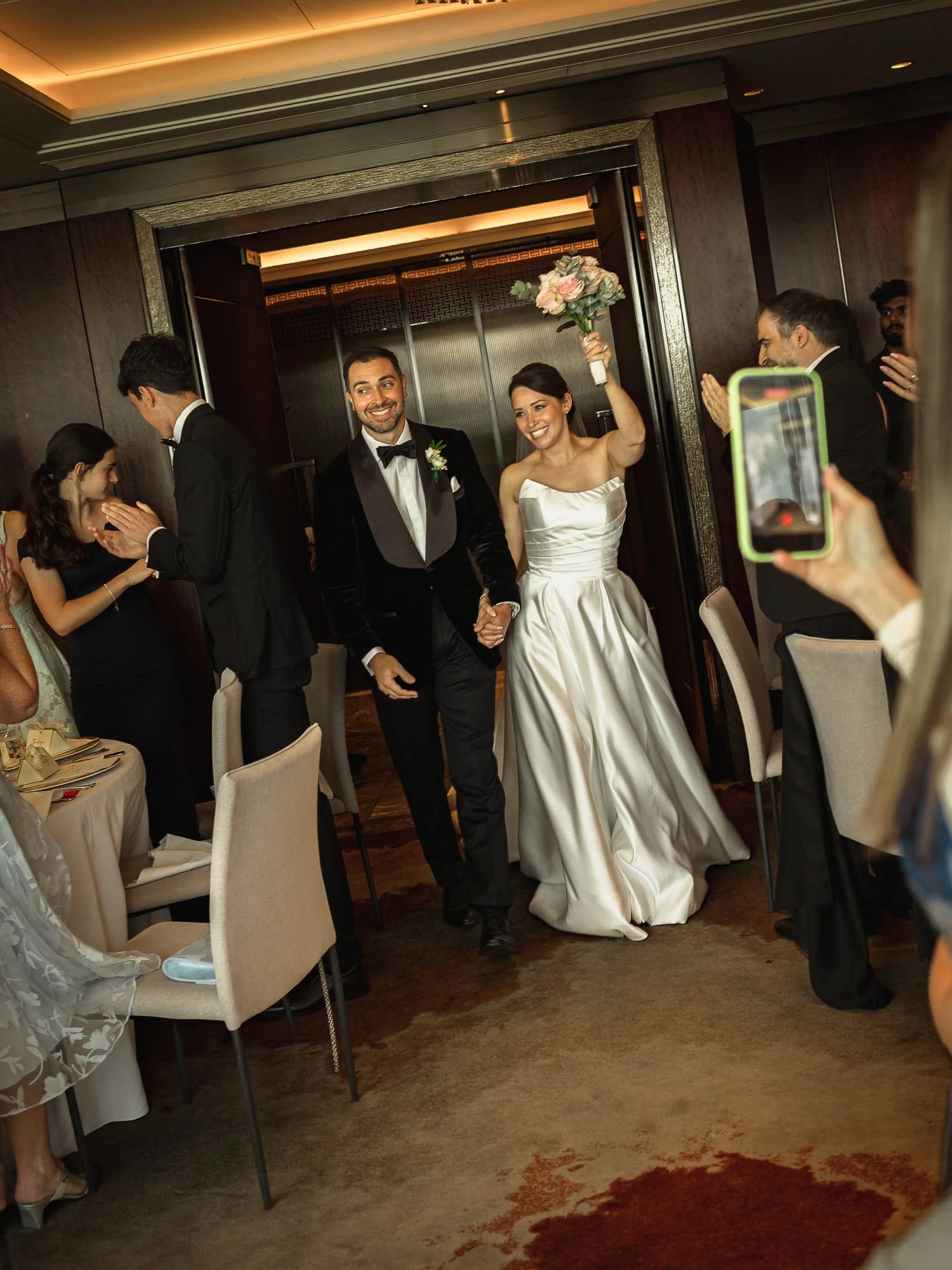 A celebratory London wedding moment as a bride and groom enter their black tie wedding reception at the Shangri-La hotel as their friends and family cheer them on.