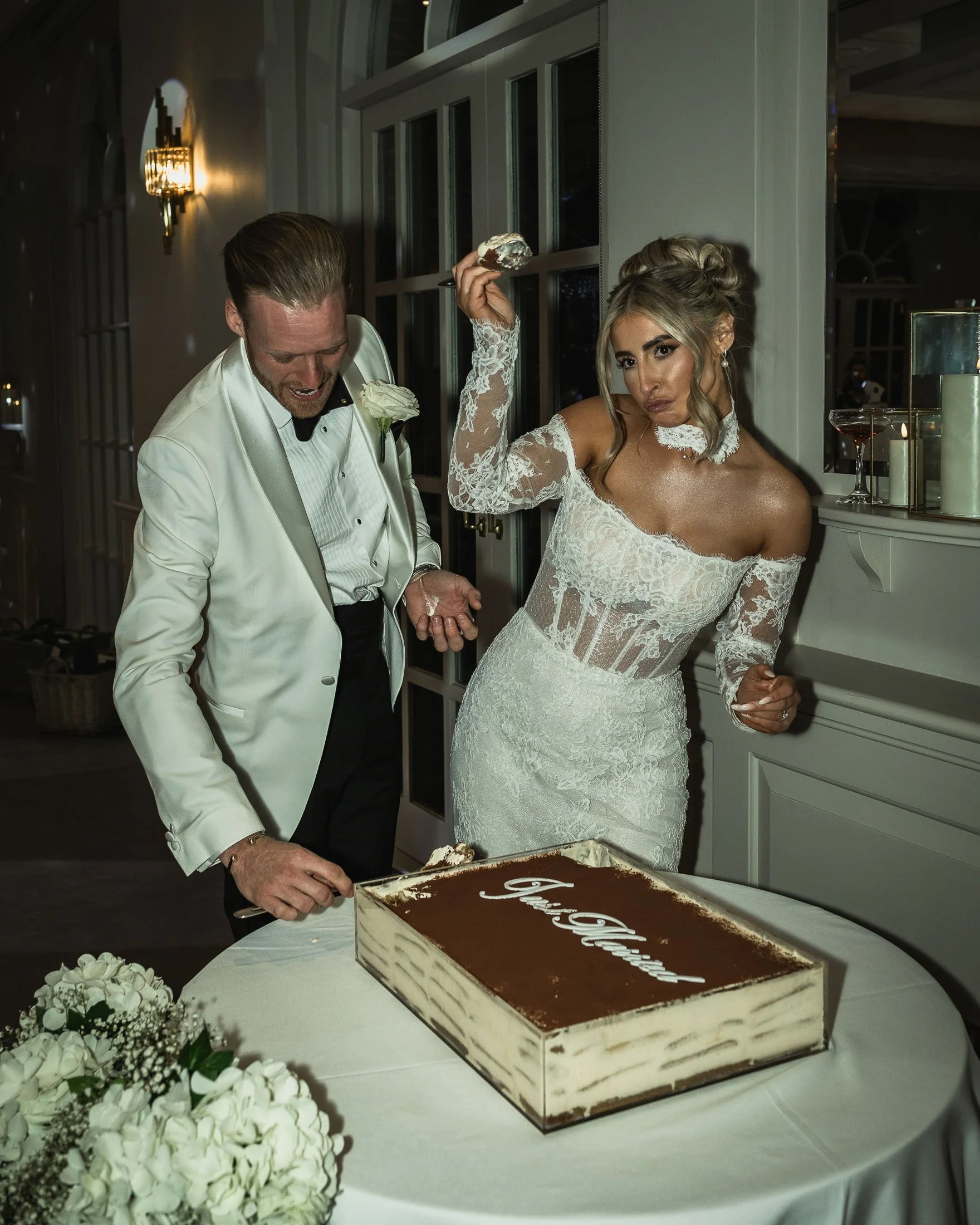 An editorial wedding photo and video team capture a bride and groom cutting a tiramisu wedding cake at The Orangery Maidstone in Kent.