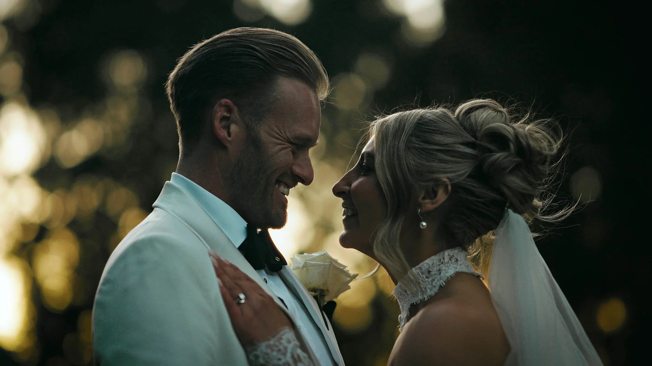 A close-up couples portrait taken at sunset, as the bride and groom laugh together.