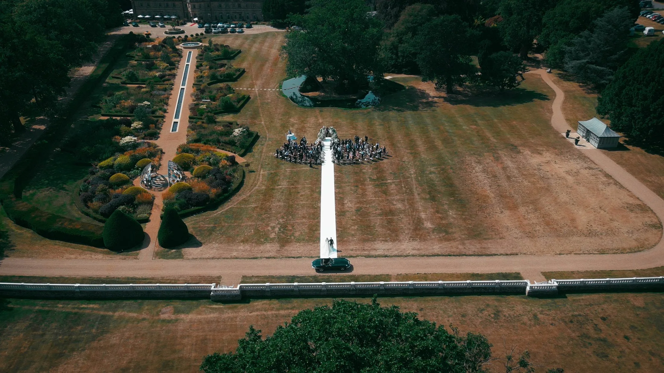 An aerial drone shot of a bride walking into her outdoor wedding ceremony on the Front Lawn of the Grantley Hall wedding venue in Yorkshire.