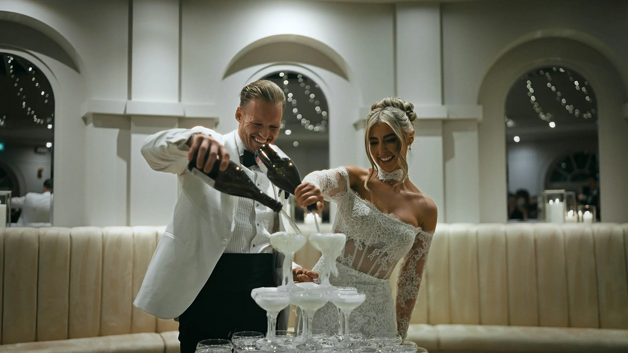A couple pouring Champagne into their Champagne tower during cocktail hour, a moment taken from their storytelling wedding film.