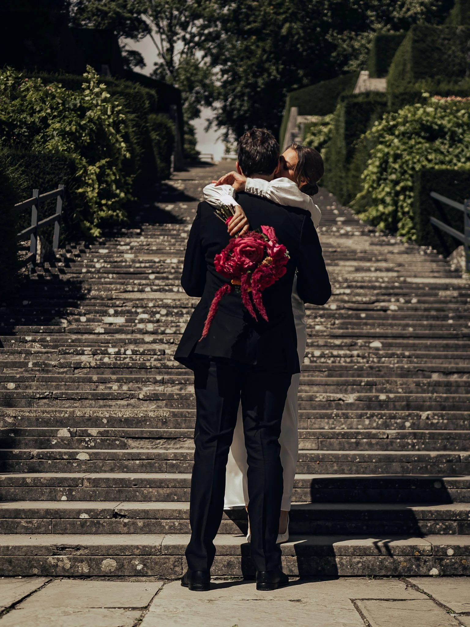 Candid couples portrait as the bride wraps her arms around the groom whilst holding a brightly coloured bouquet.