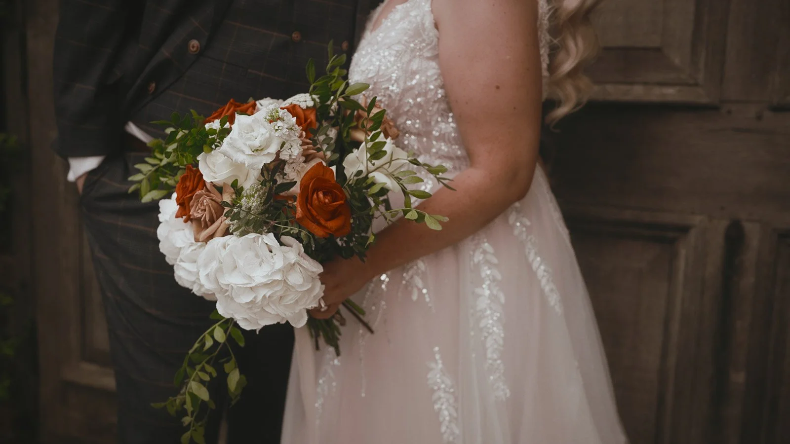 Details of the brides orange and white colourful bouquet in a Winters Barns wedding film.