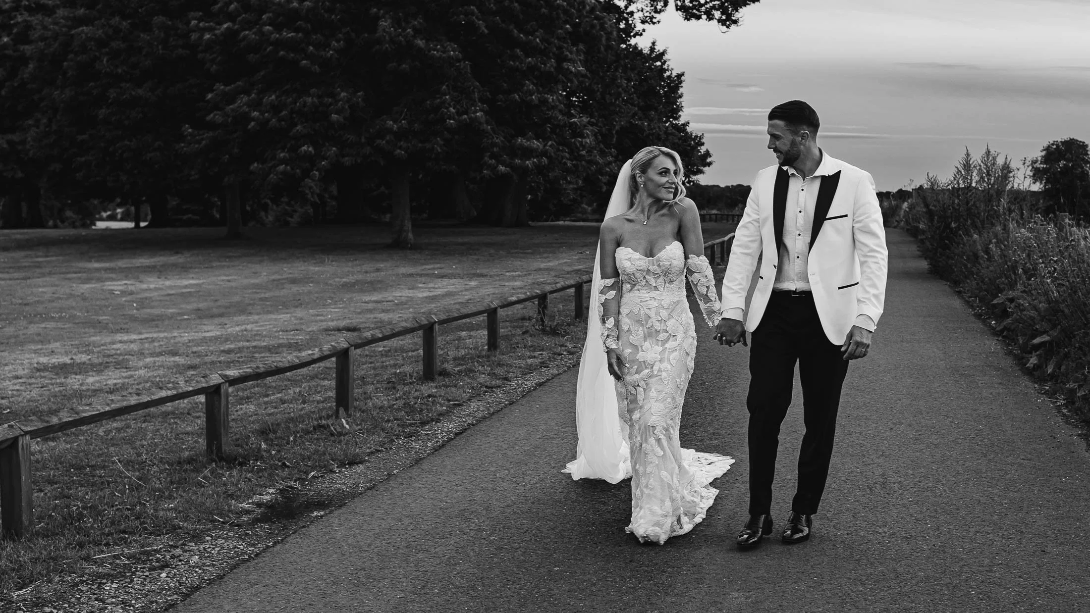 A black and white editorial image of a couple walking holding hands, whsilt being captured by both photo and video on their wedding day in Kent