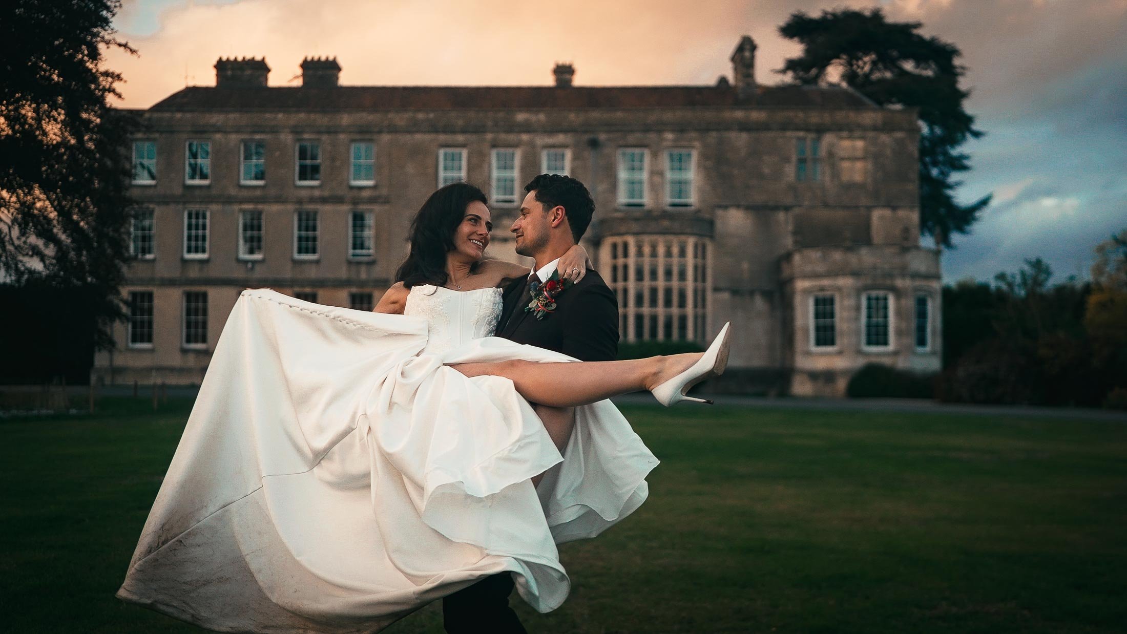 Groom picks up bride with Elmore Court in the background.