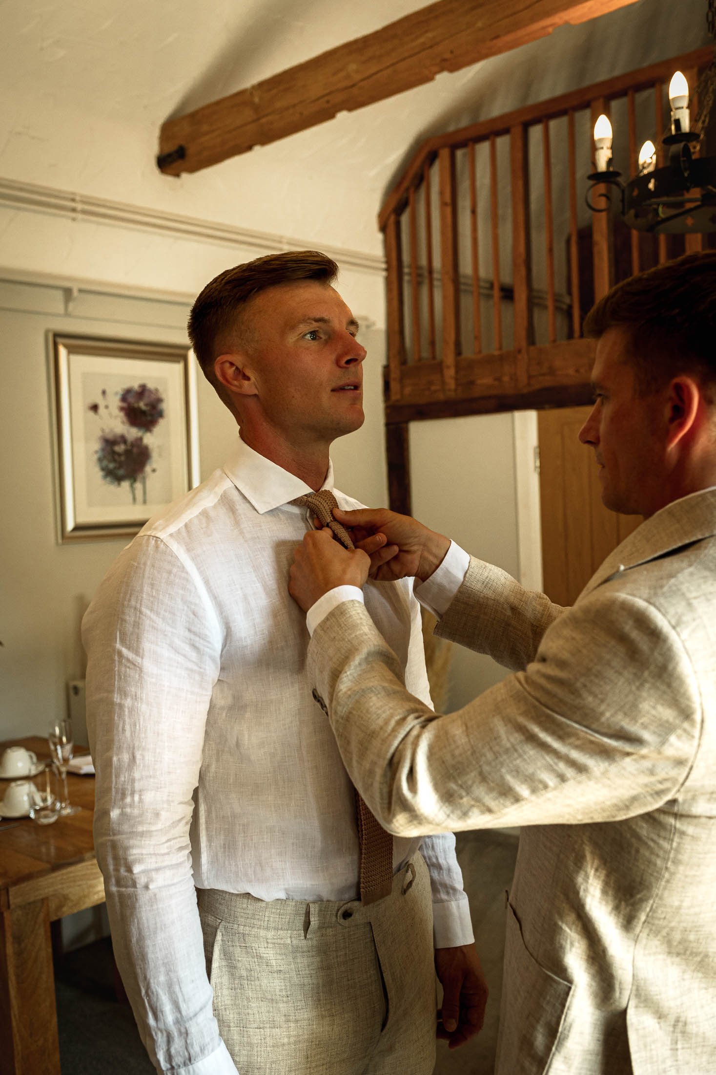 A candid wedding moment as the Best Man fixes the tie of the Groom during morning preparations at Winters Barns.