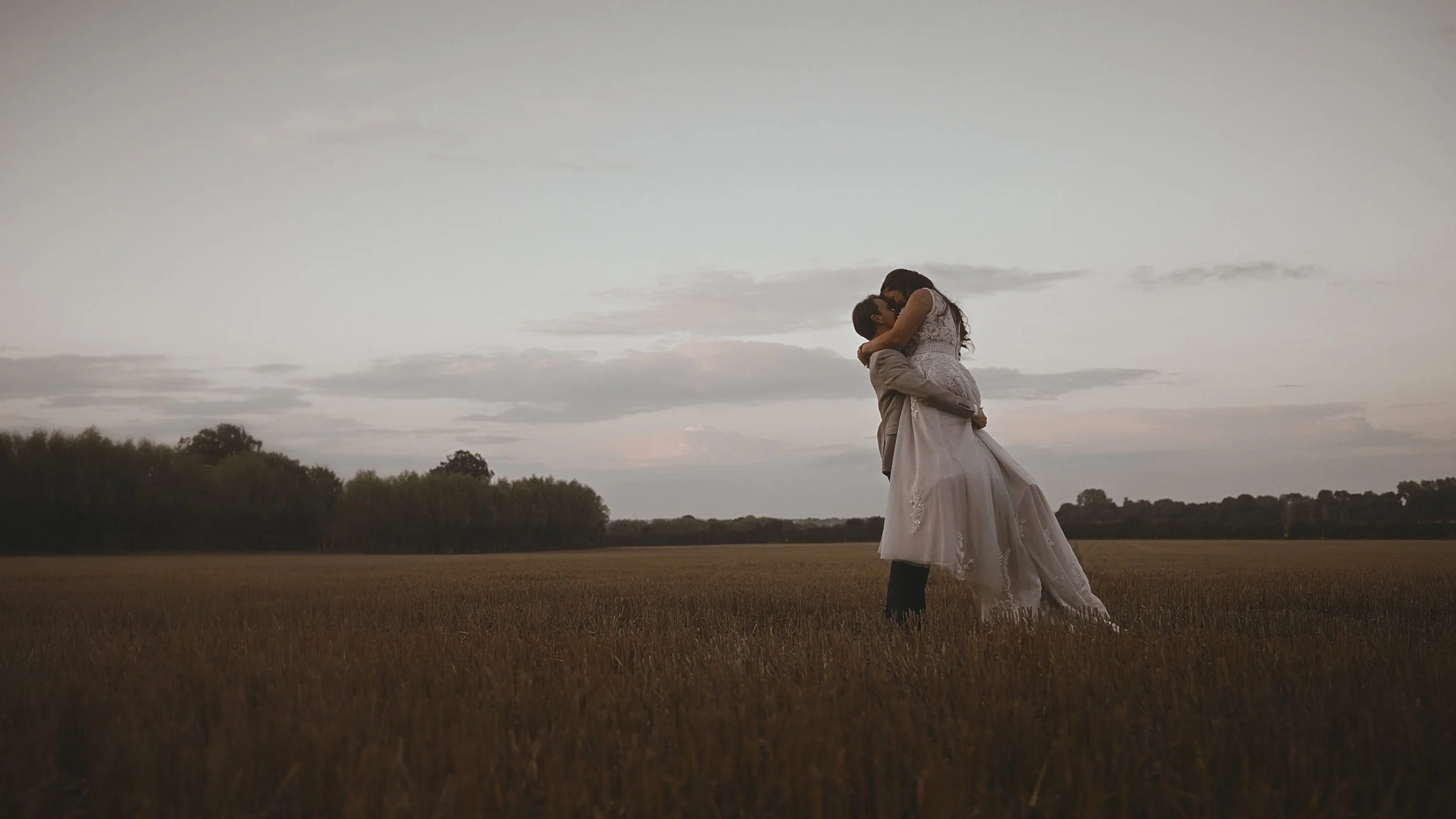 A groom lifts his bride in an open field during golden hour sunset shots at a September wedding at Winters Barns, Kent.