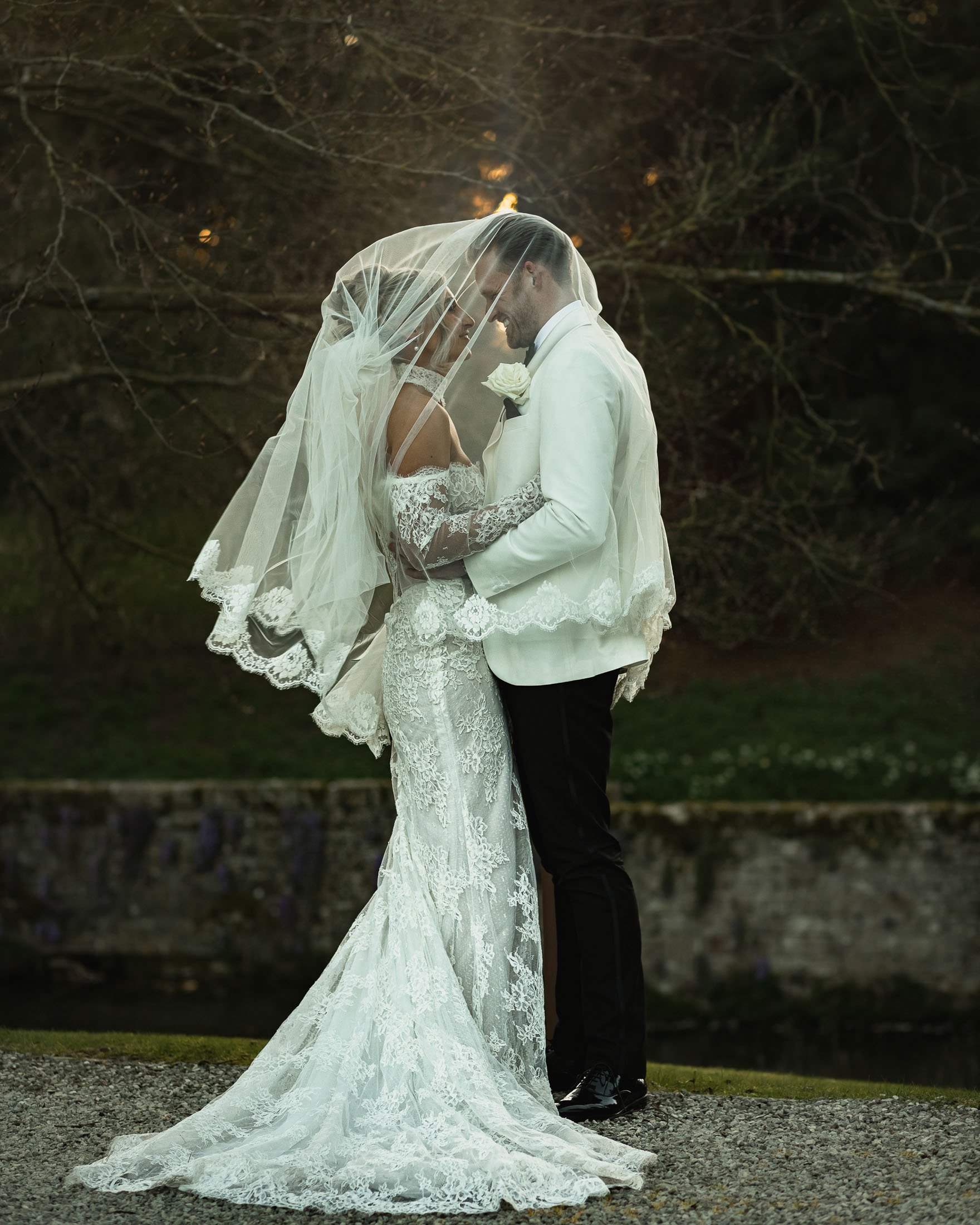 An editorial couple pose as the bride and groom stand underneath a veil at sunset at the Orangery Maidstone in a moment captured by photo and film.