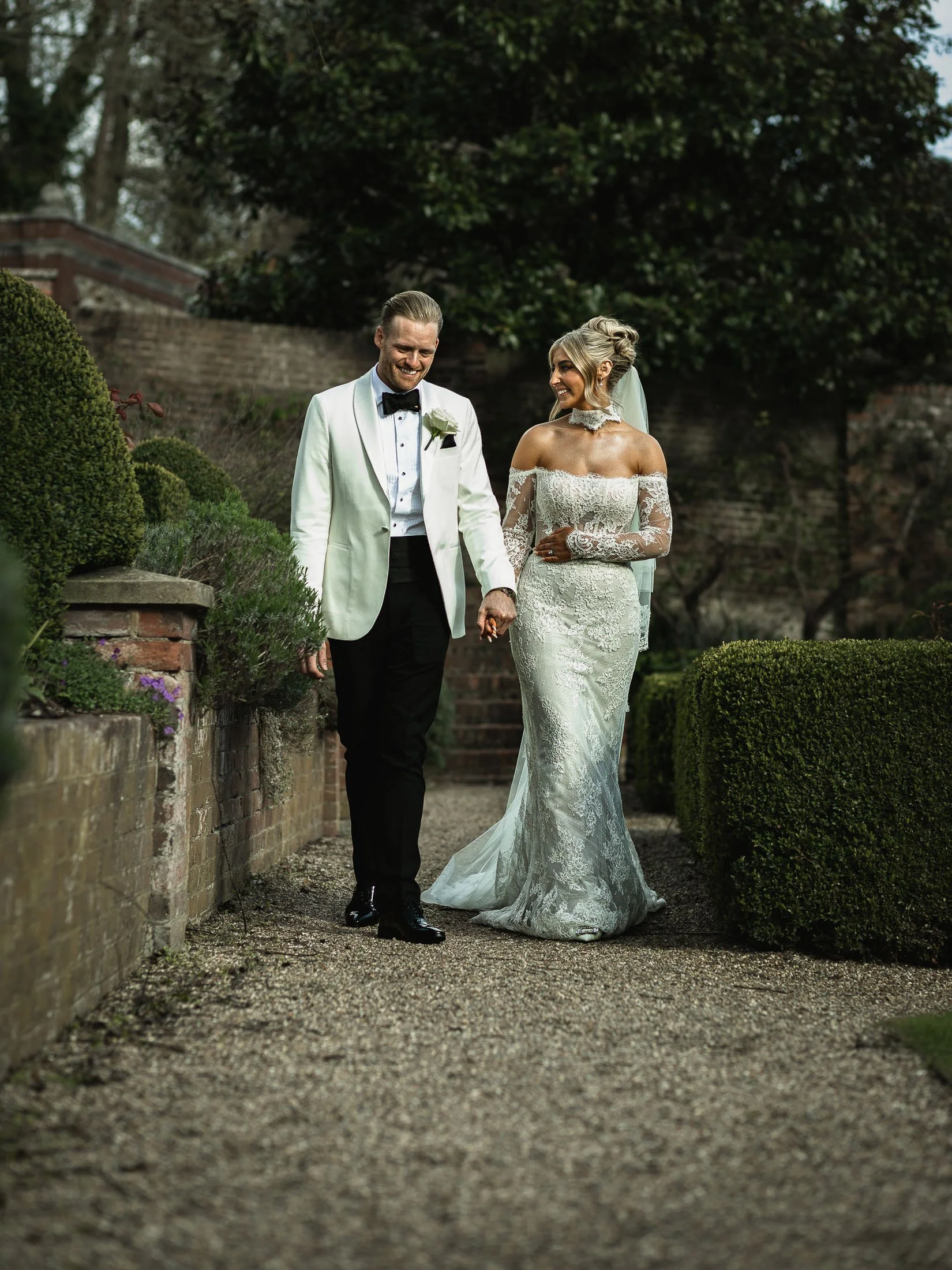 A bride and groom in white tuxedo walk through the grounds of The Orangery Maidstone.