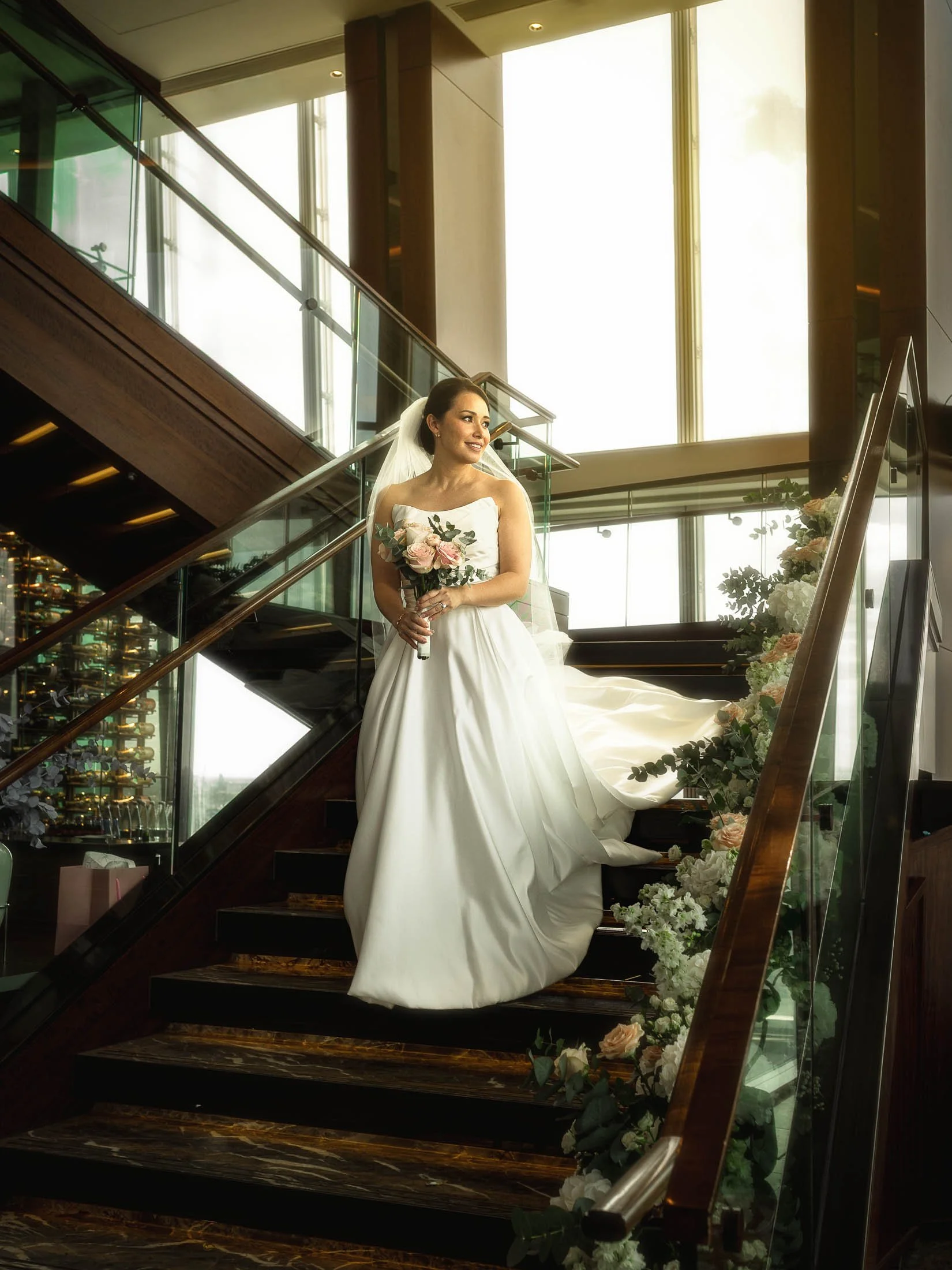 An editorial bridal portrait of a bride walking down the staircase at the Shangri-La The Shard hotel in London, as she is captured by editorial wedding photography and cinematic wedding videography.