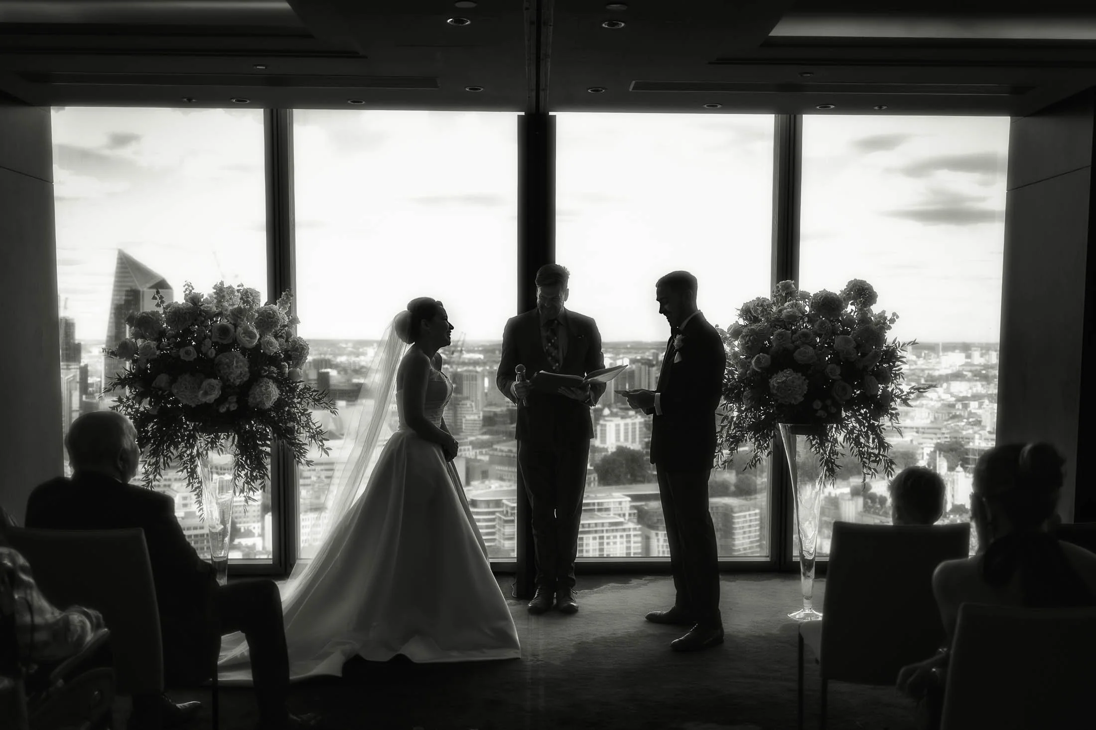 An indoor wedding ceremony at Shangri-La The Shard as the bride and groom are silhouetted against the city backdrop.