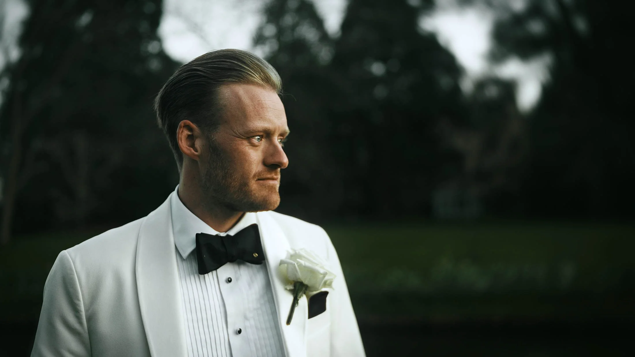 A close up cinematic style portrait of a groom in black tie white tuxedo during golden hour at The Orangery, Maidstone, forming part of a storytelling wedding film in the UK.