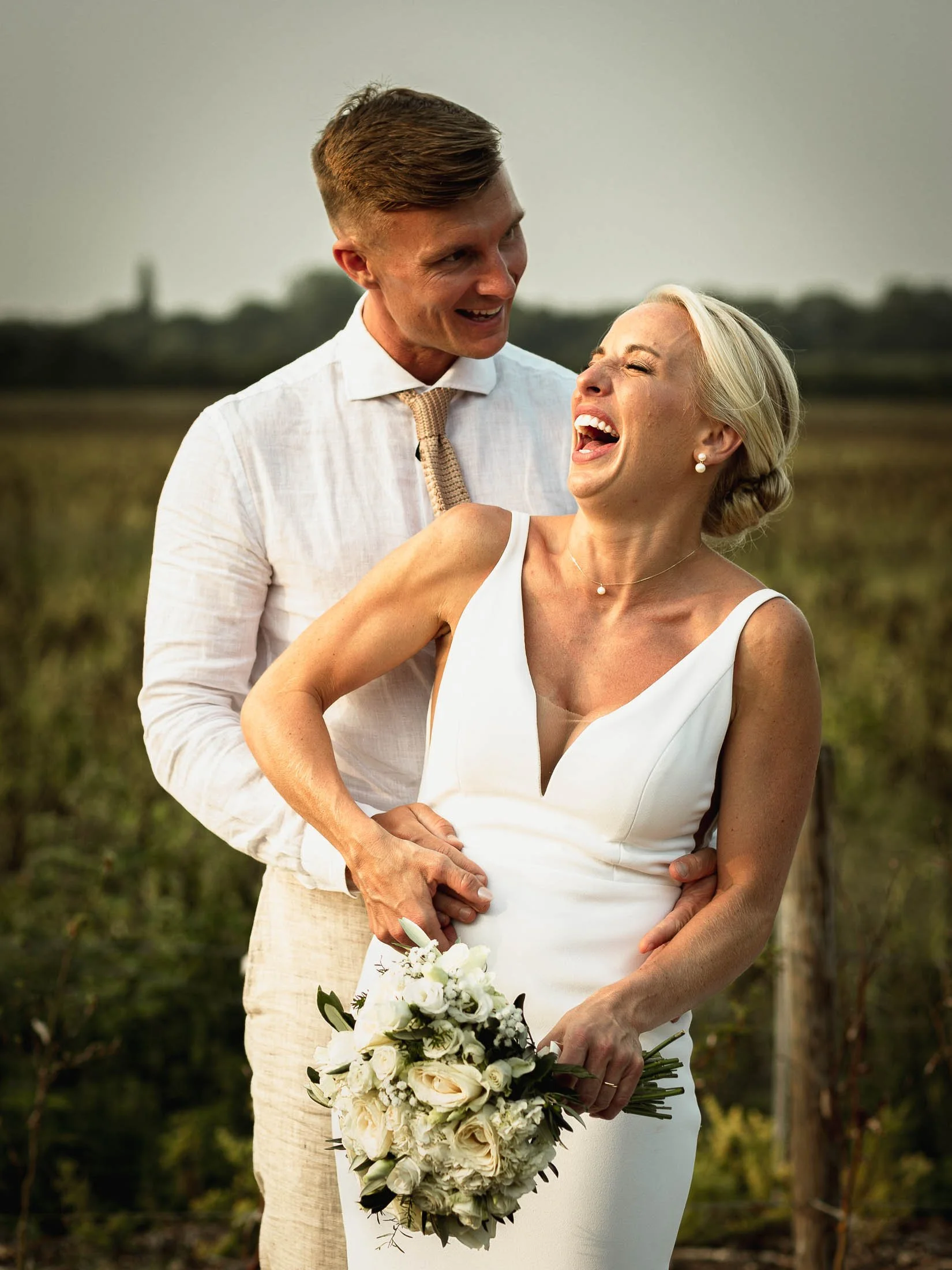 A natural moment as a bride and groom laugh heavily together during their summer wedding day, captured at Winters Barns in Kent.