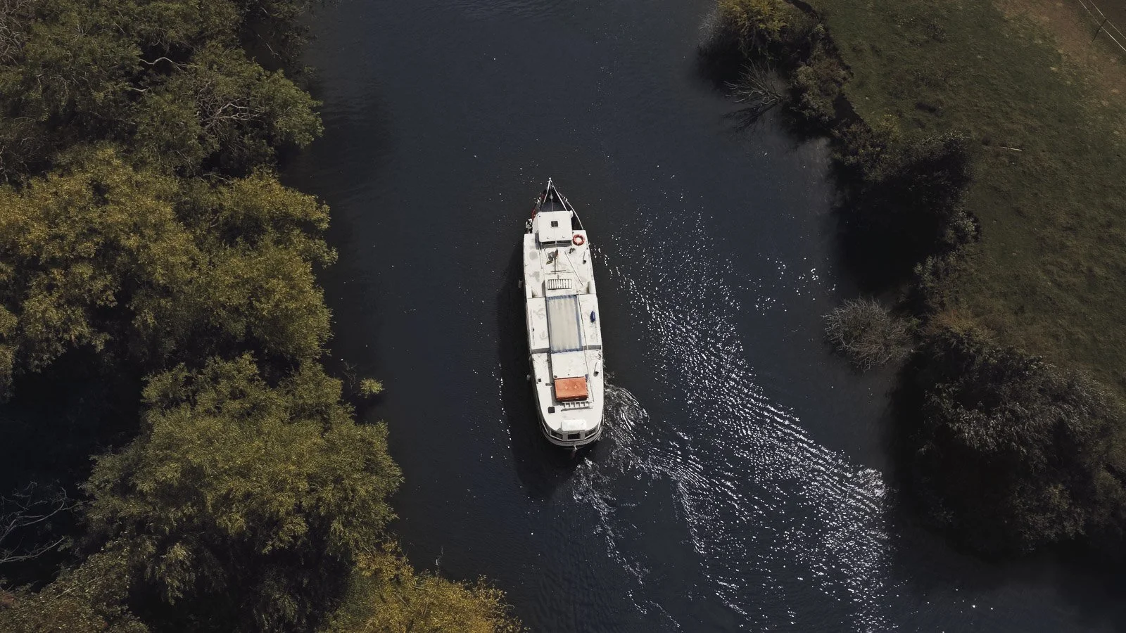 An aerial image of a bride travelling to her colourful riverside wedding ceremony by boat along the River Thames.