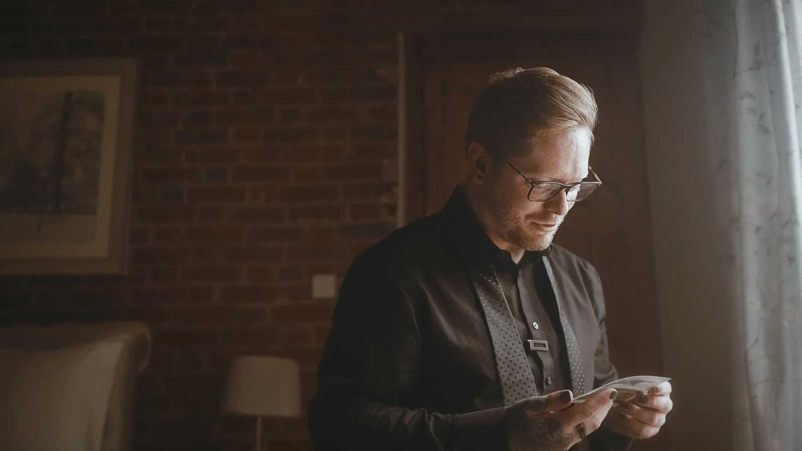 Groom reading an emotional letter in soft window light on wedding morning