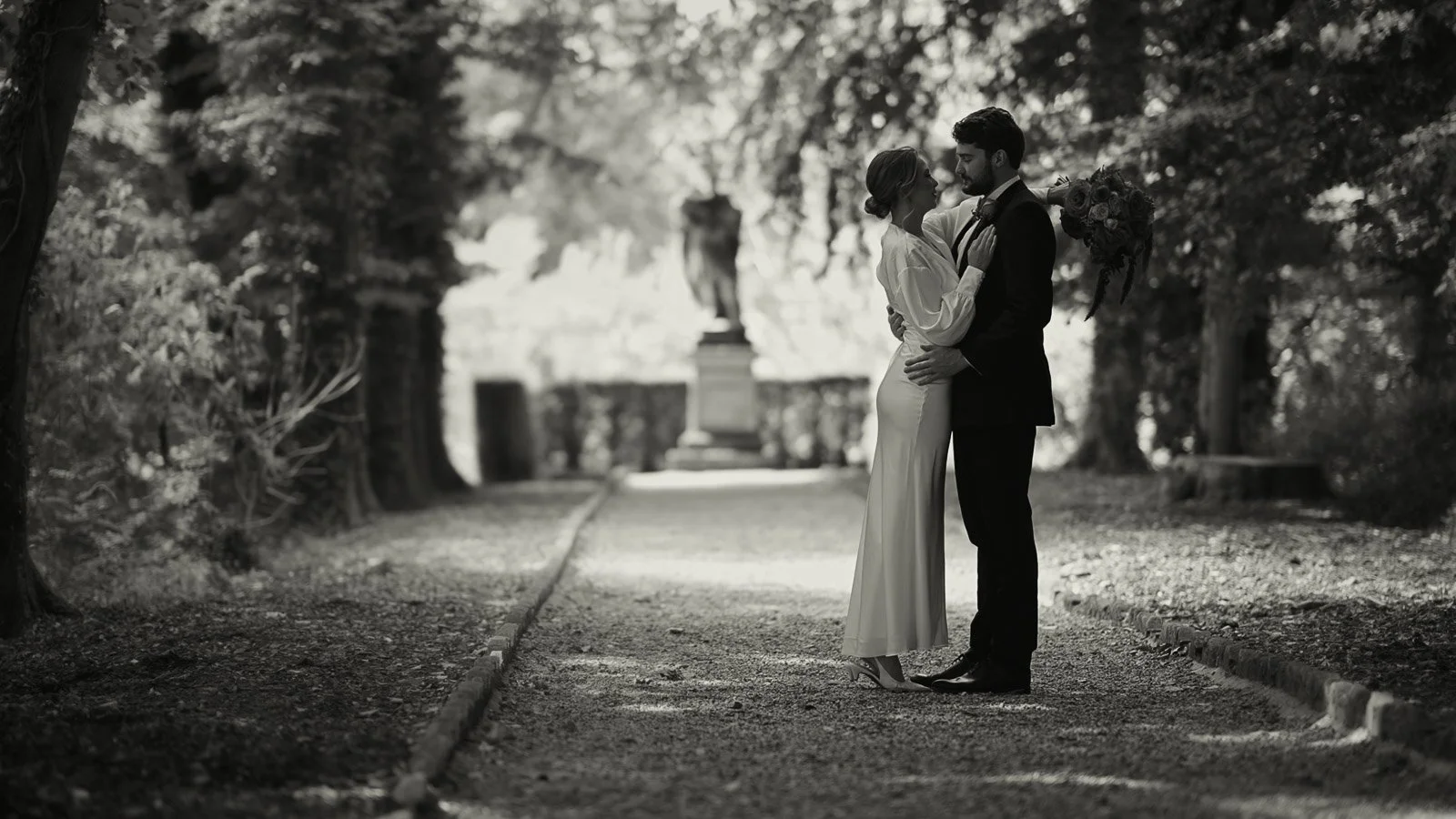 A fine art wedding moment as a couple are framed by a long path and woodland.