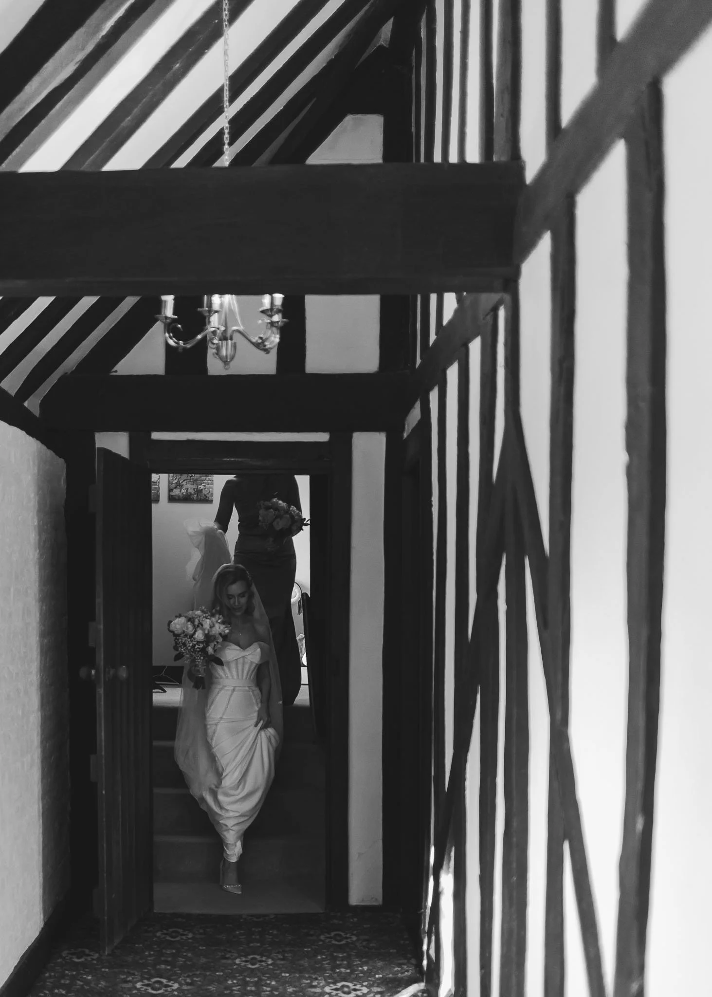 A black and white image of a bride walking through a corridor at Leez Priory in Essex as she is captured by a wedding photo and video team.