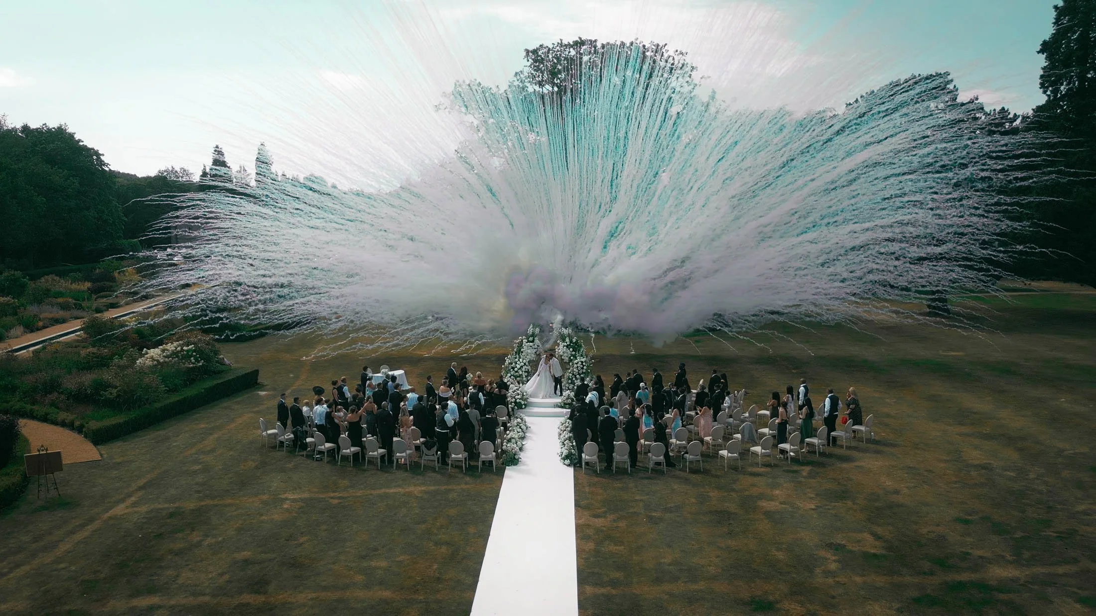 A drone shot of daytime fireworks exploding during a summer outdoor wedding ceremony at Grantley Hall, Yorkshire.