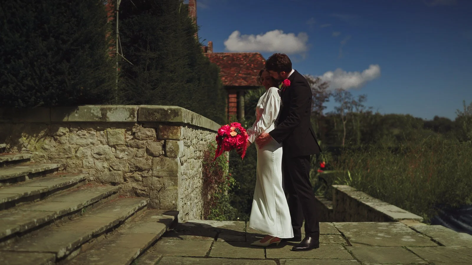 An editorial moment during a colourful black tie wedding as a groom wraps hi arms around his bride during the summer.