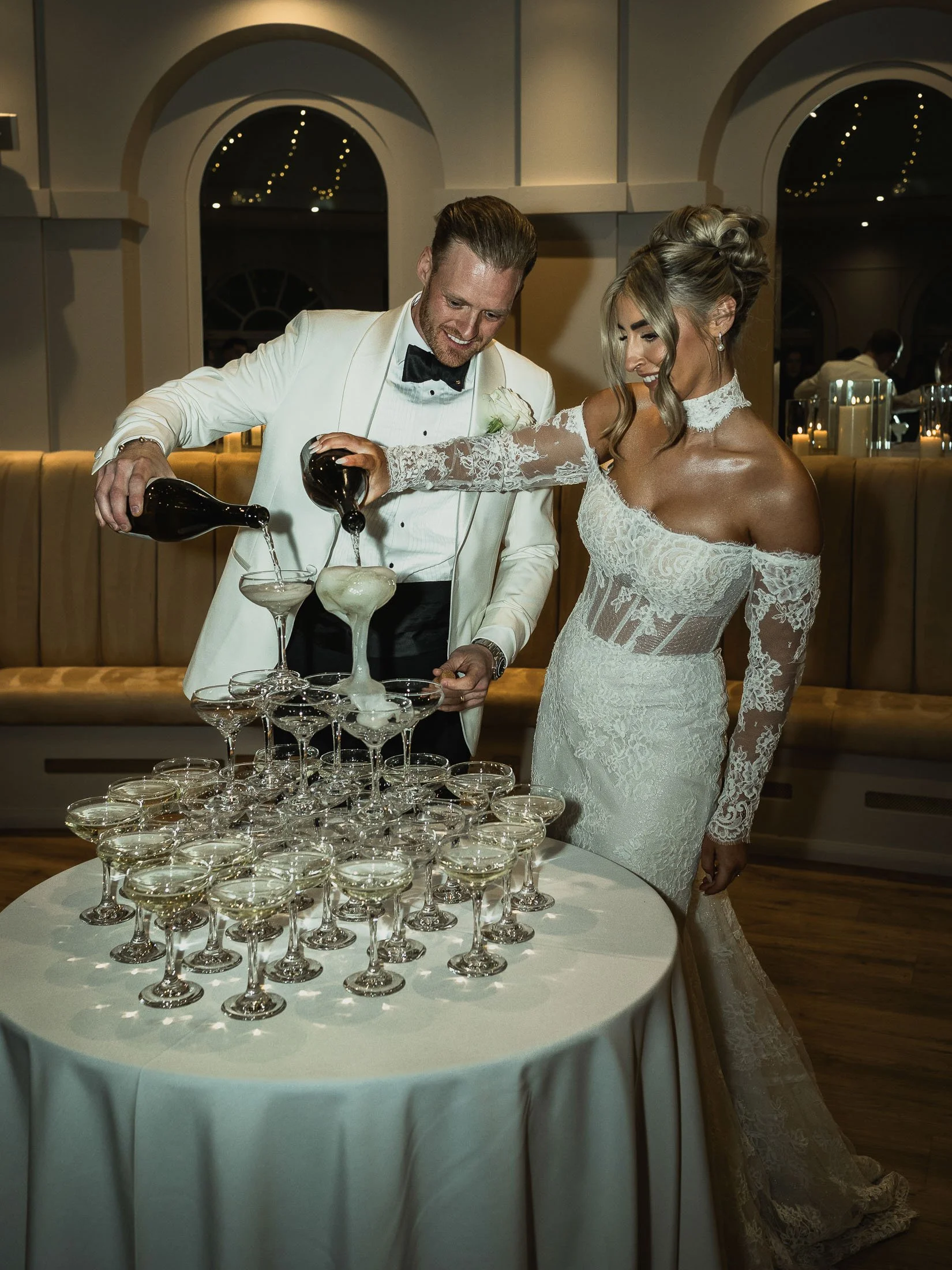 An editorial flash-photography image of a bride and groom pouring a Champagne tower at The orangery Maidstone.