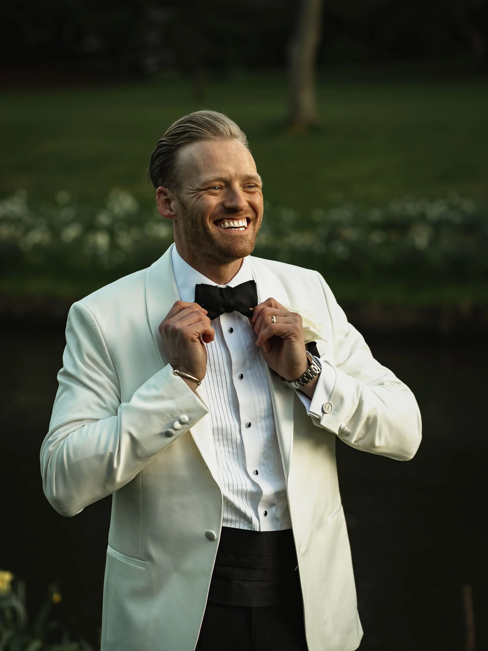 A candid moment of a groom in white tuxedo  adjusting his bow tie during his black-tie wedding at The orangery Maidstone.