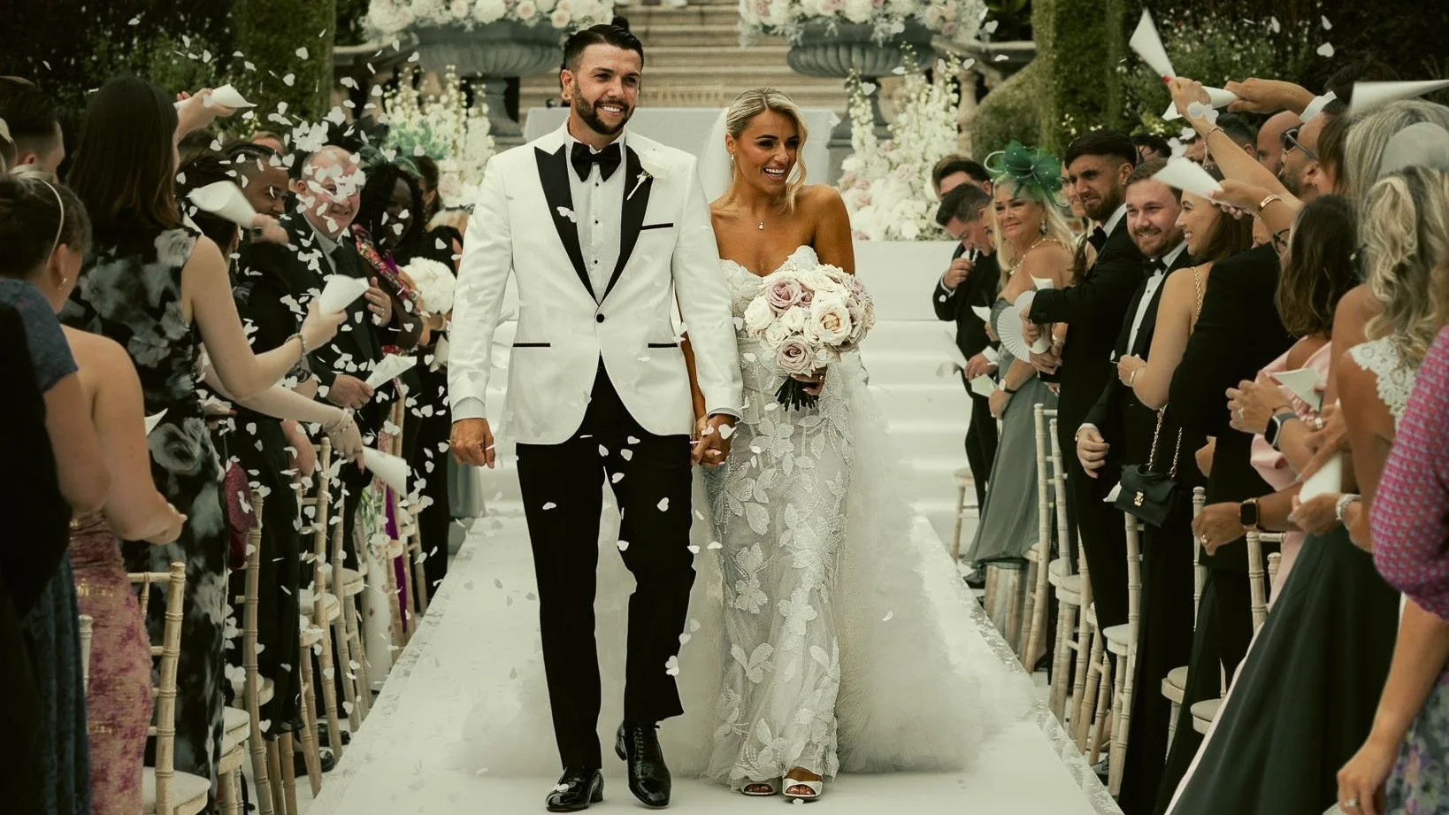 A couple exiting their outdoor wedding ceremony are showered with large, luxurious confetti in a moment from a destination wedding film.