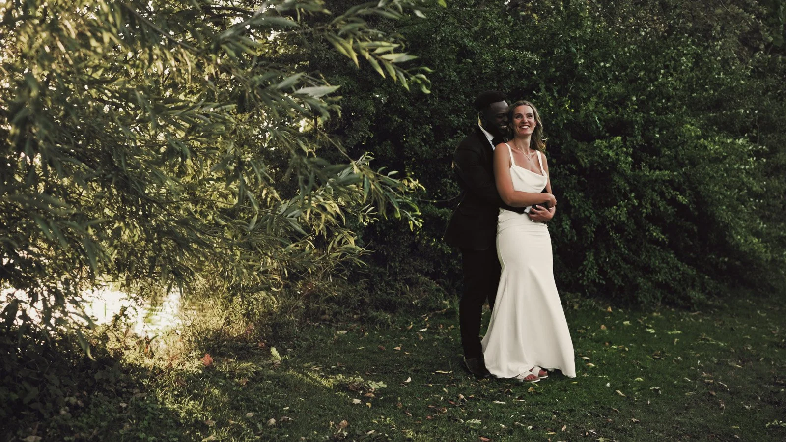 a couple embrace each other on the banks of the river Thames during a quiet moment in their riverside wedding video.