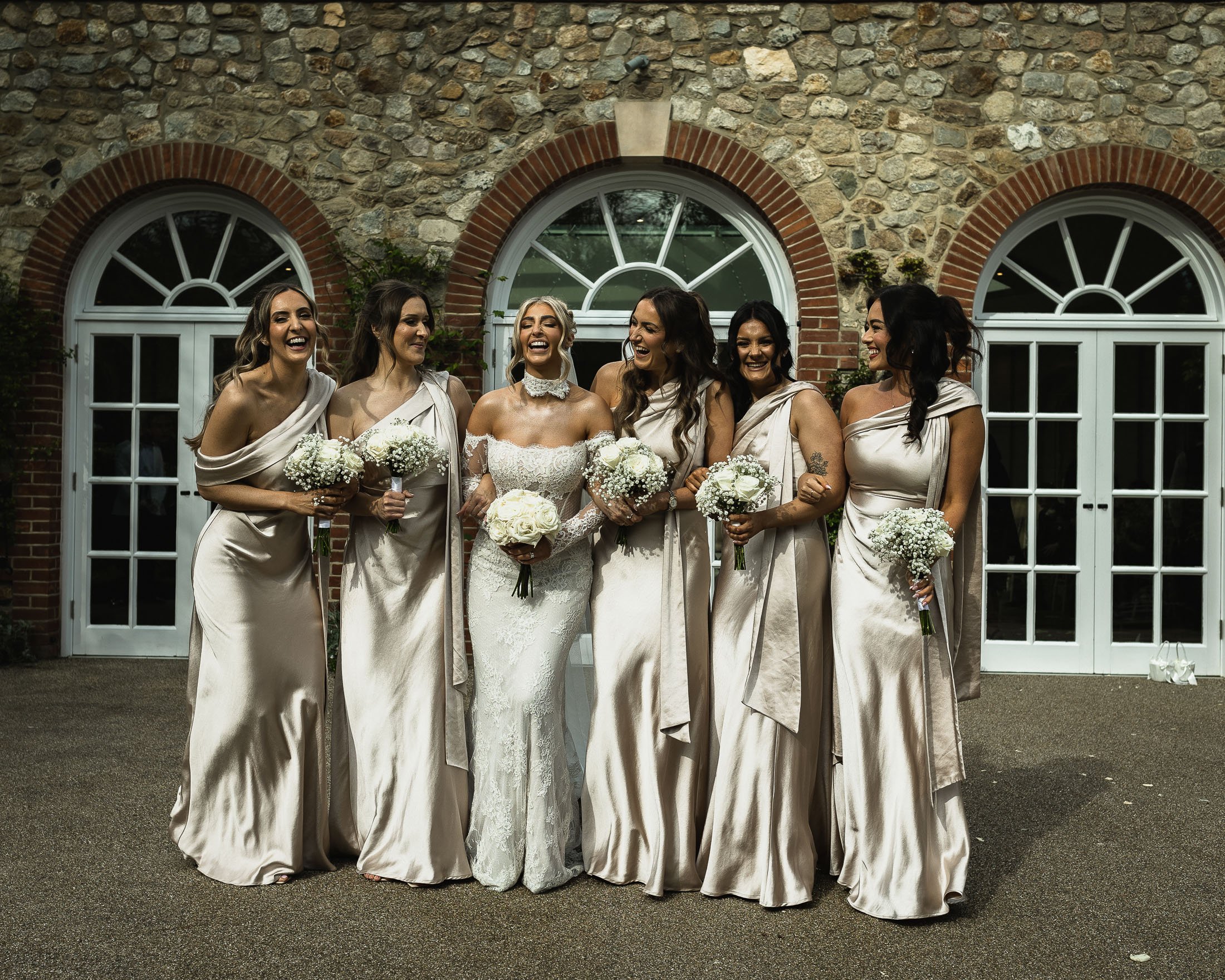 A bride in a Millanova wedding gown walks with her bridesmaids wearing Champagne coloured dresses at The Orangery Maidstone in Kent.