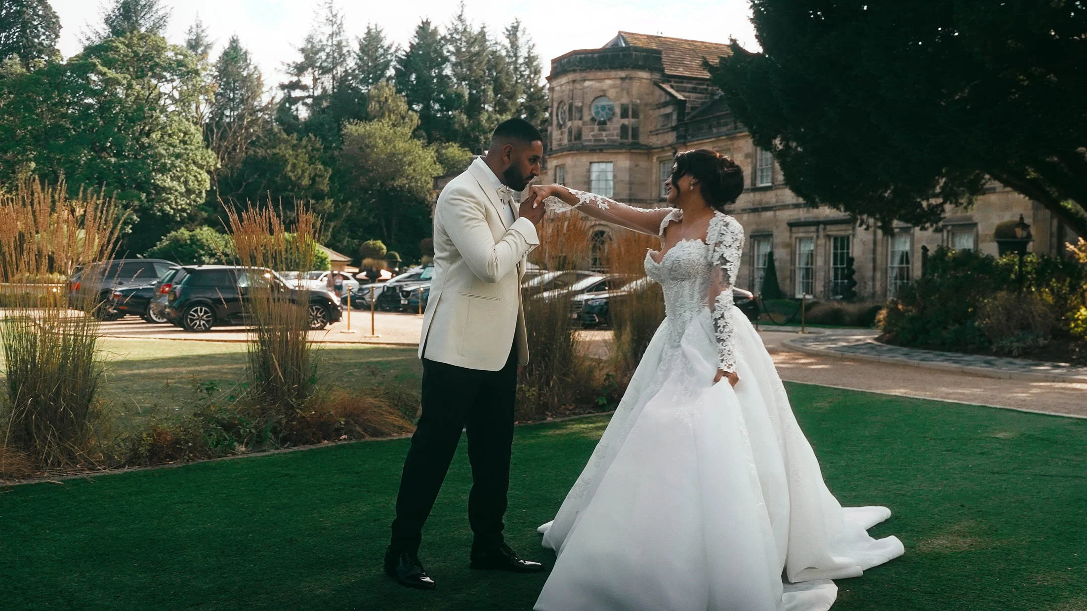 The groom kisses the hand of his wife during a black tie wedding film at Grantley Hall, Yorkshire.