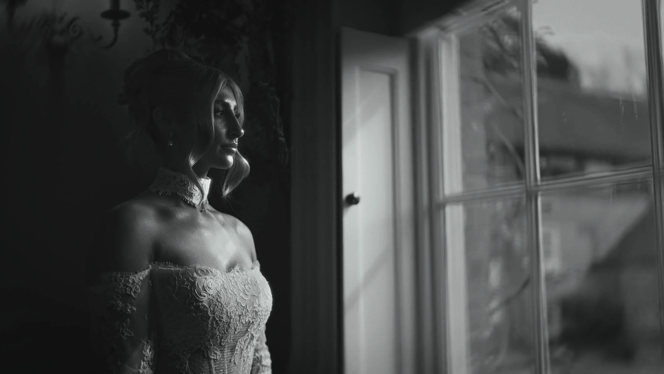 A cinematic style black and white bridal portrait by a large window, captured as part of a storytelling wedding film in the UK.