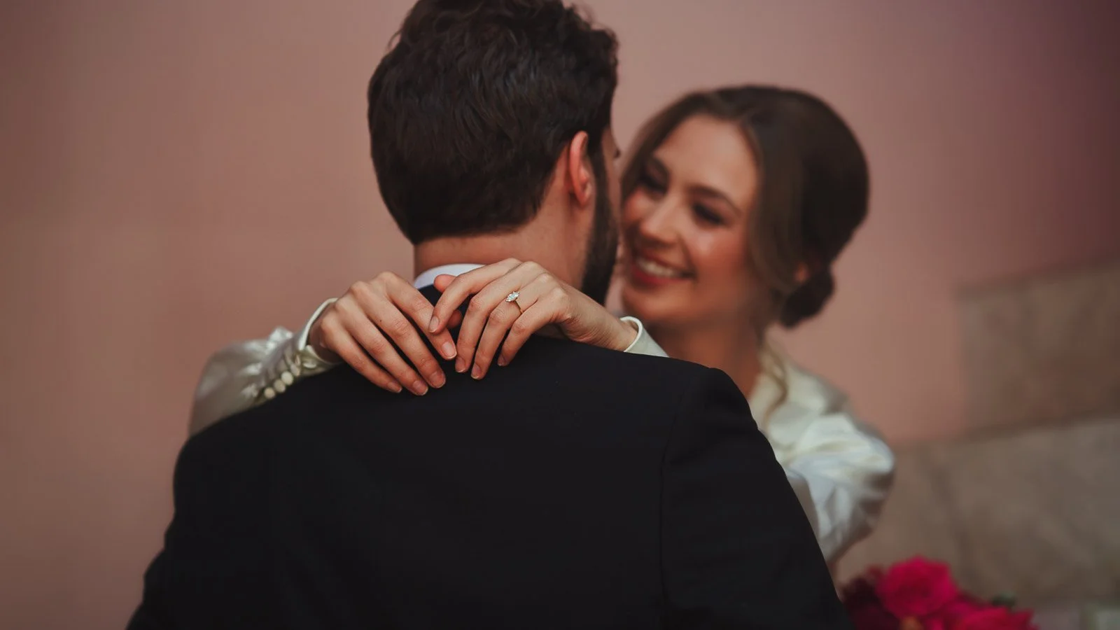 A bride wraps her hands around the grooms neck whilst showing her wedding ring in an editorial wedding film moment.