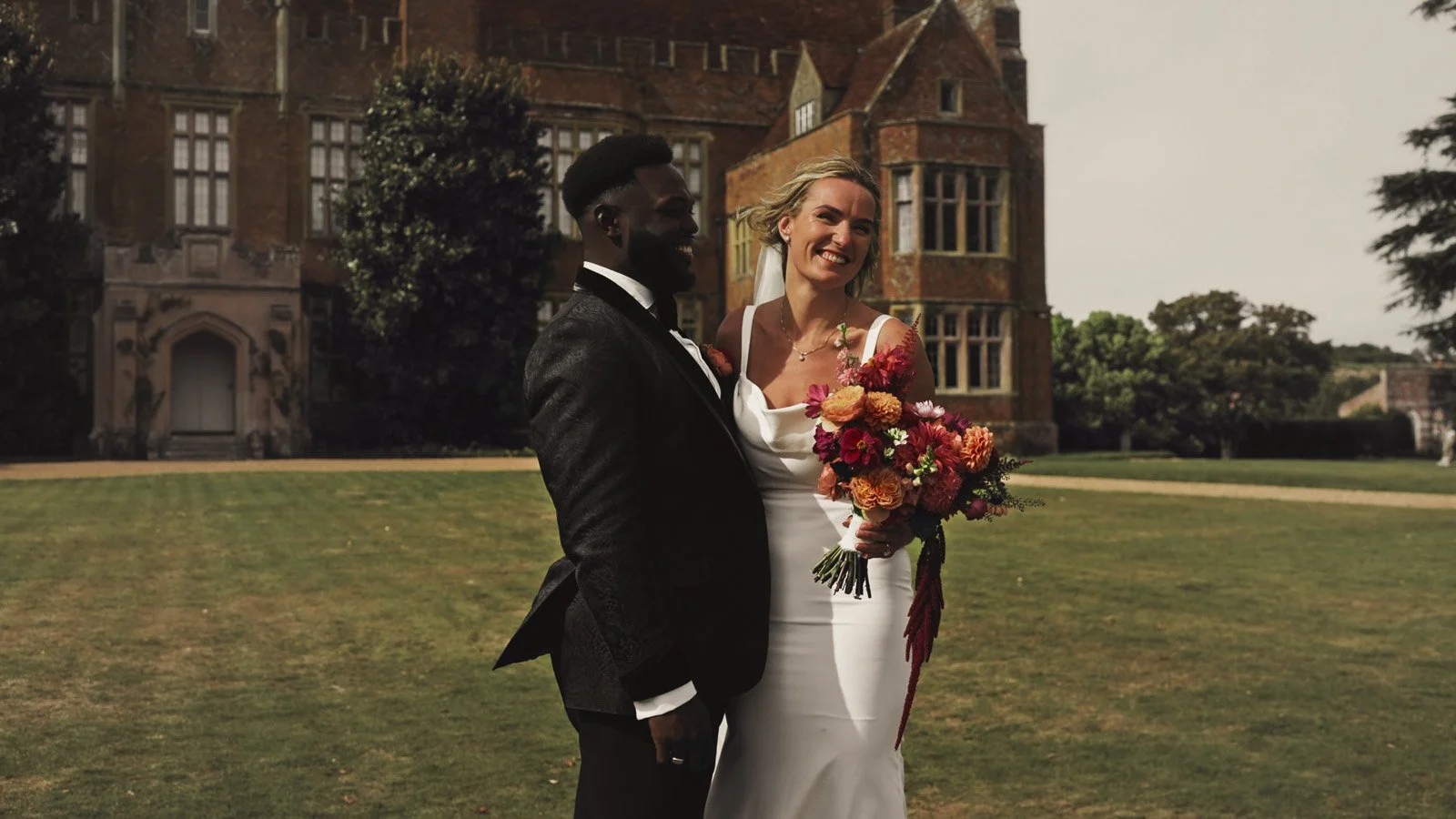 A couple stand together on the driveway of an Oxfordshire Estate during their colourful riverside wedding day.