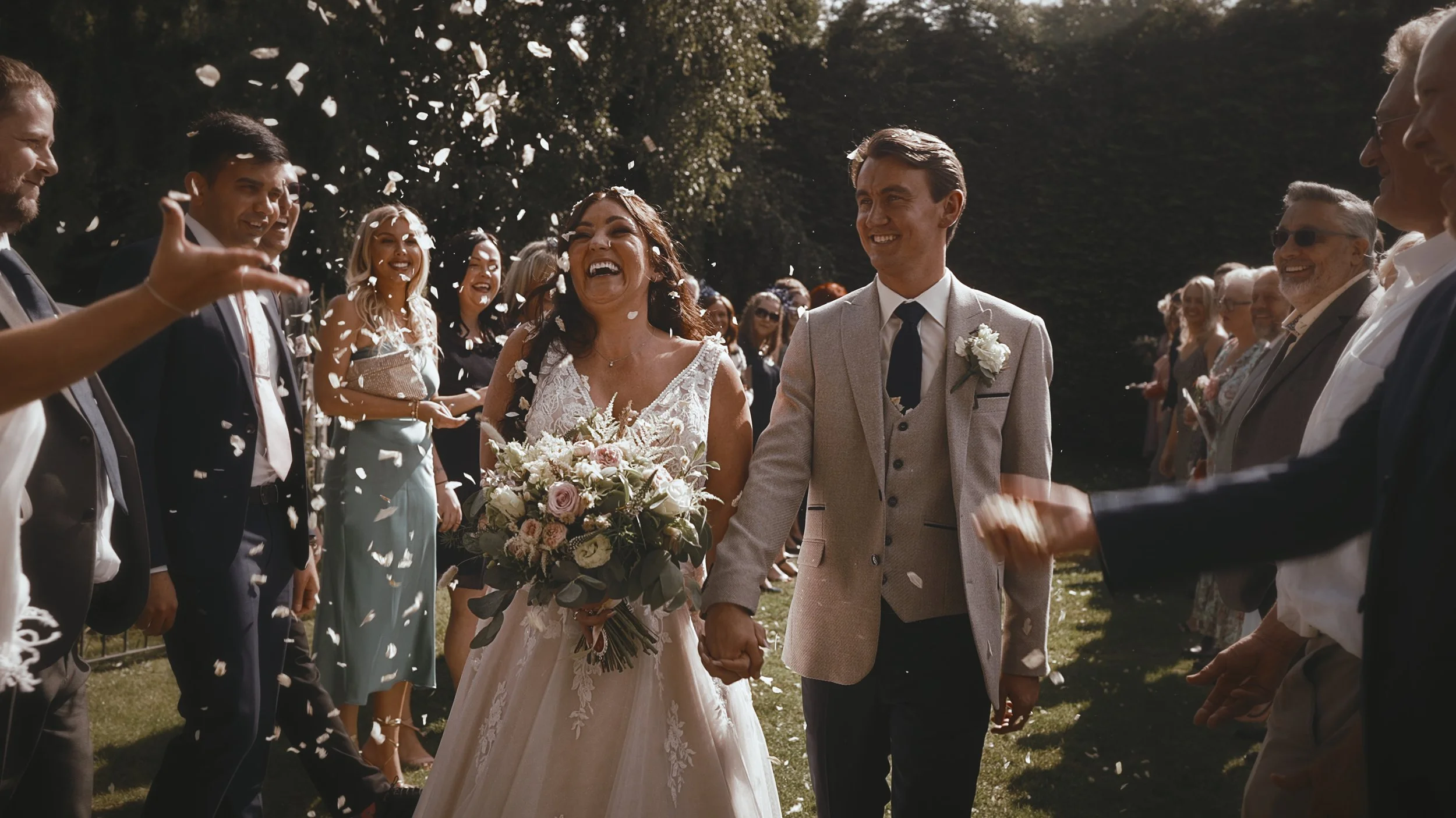A bride and groom during their confetti walk, framed editorially fro a cinematic wedding film.