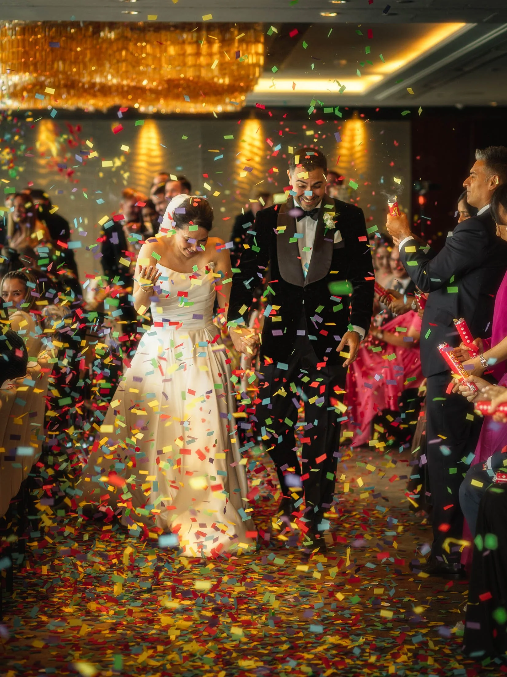 A happy moment during a black tie London wedding at the Shangri-La The Shard, as a bride and groom exit their wedding ceremony under a sea of multi-coloured paper confetti.