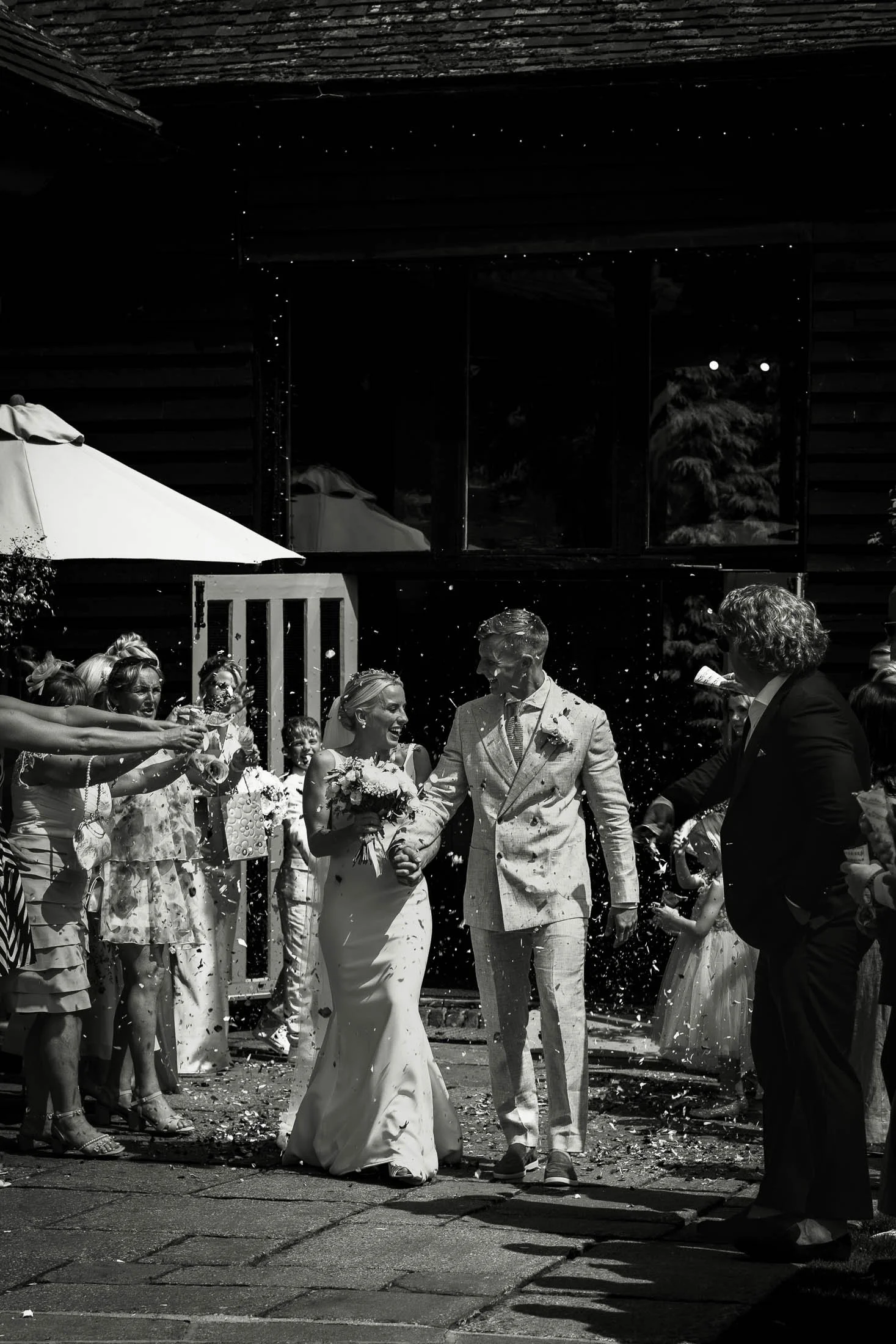 A black and white photograph showing a wedding ceremony exit of a bride and groom with confetti at the Winters Barns wedding venue in Kent.