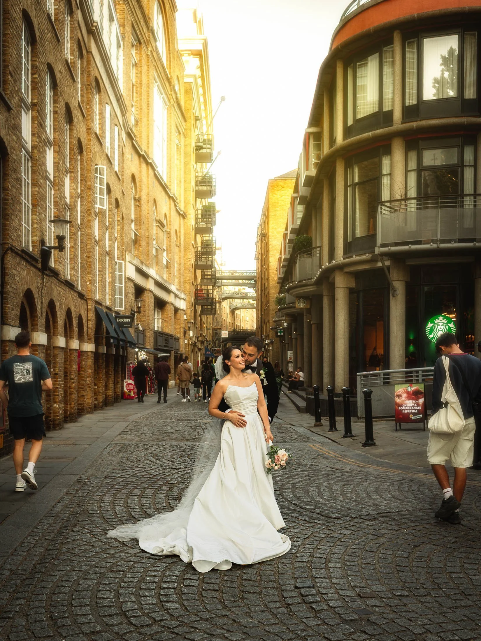 A bride and groom embrace on a cobbled street in London during their black tie wedding day couples portrait session.