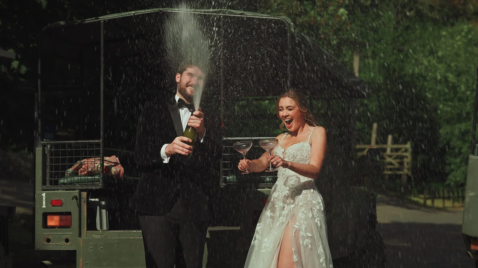 A candid moment as the groom wearing black tie opens Champagne and sprays it from the bottle.