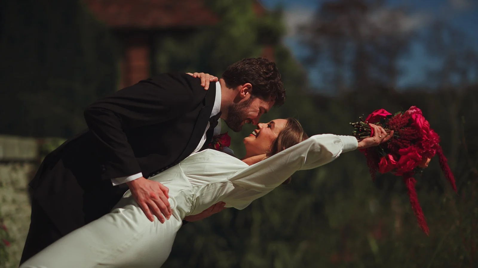 A colourful fine art wedding film moment as a couple dip and kiss during their black tie wedding.