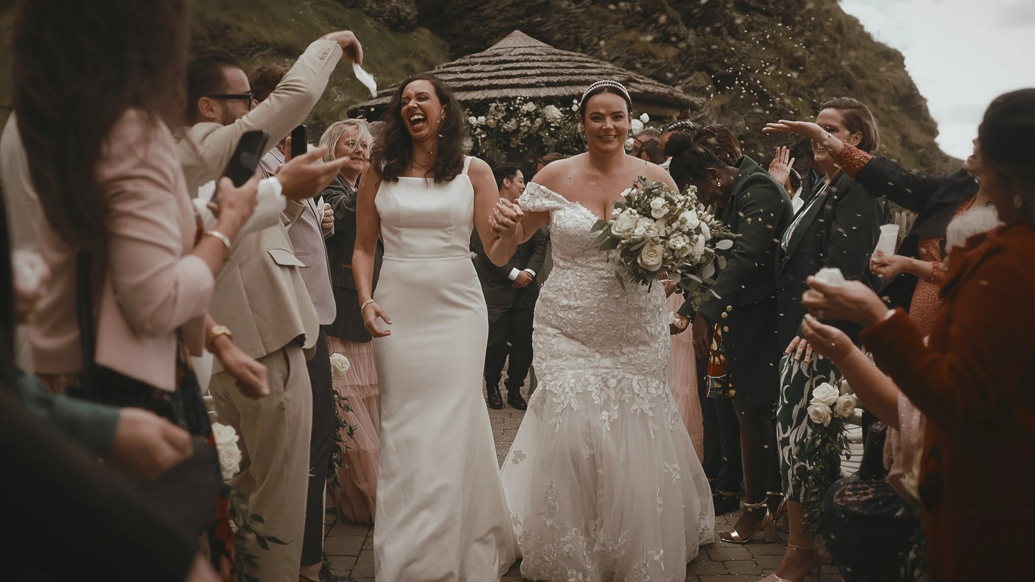 Two brides laugh as they exit their outdoor summer wedding ceremony at The Tunnels Beaches