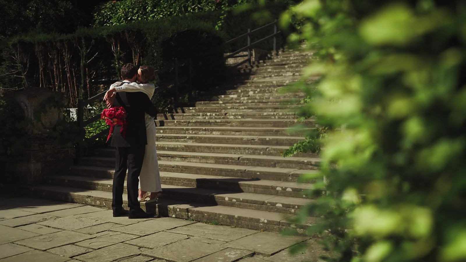A couple stand at the bottom of a stone staircase in a fashion-led portrait.
