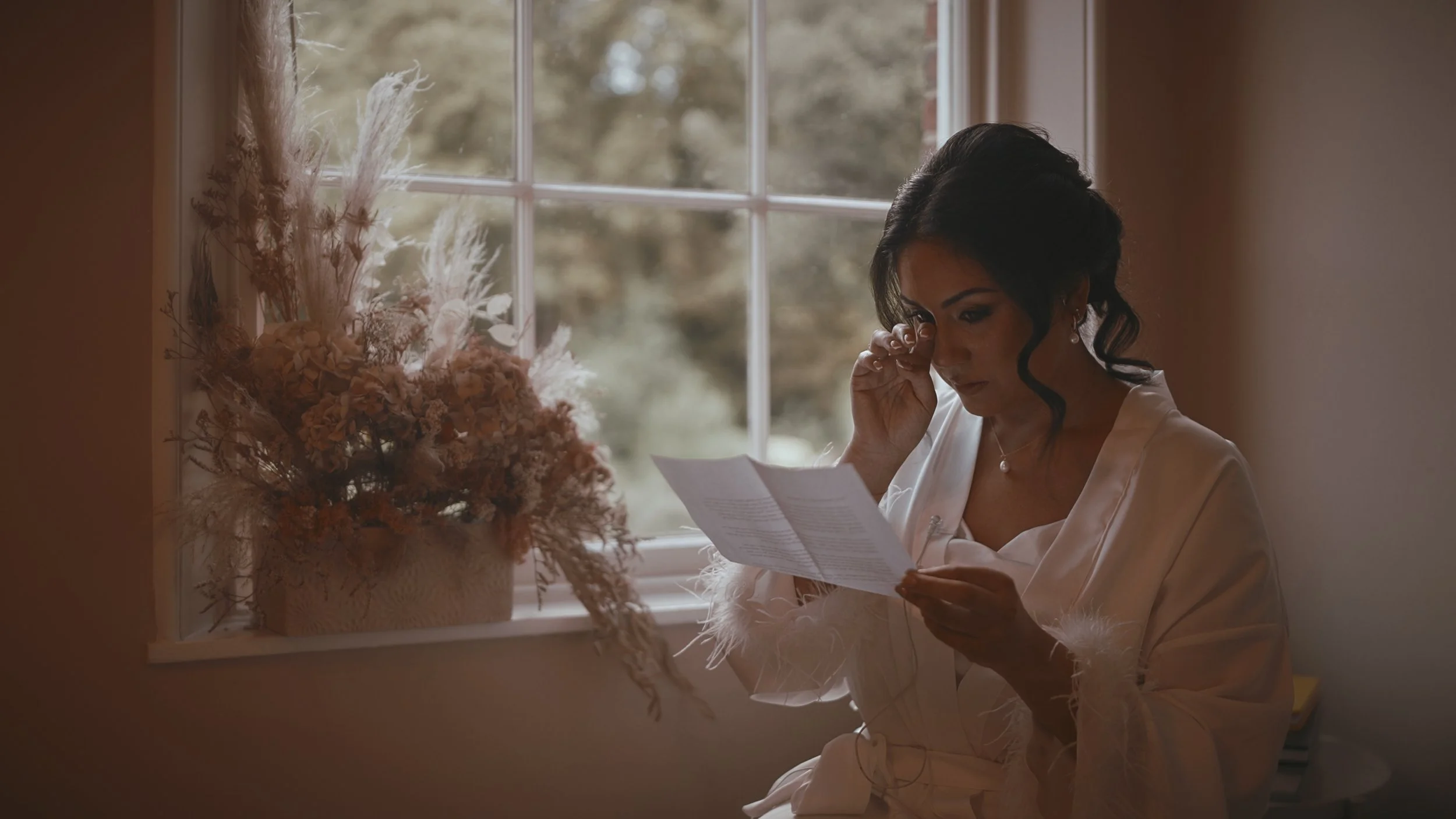 An emotional bride wipes a tear from her eye as she reads a letter from the groom on her wedding morning at The orangery, Maidstone in Kent.
