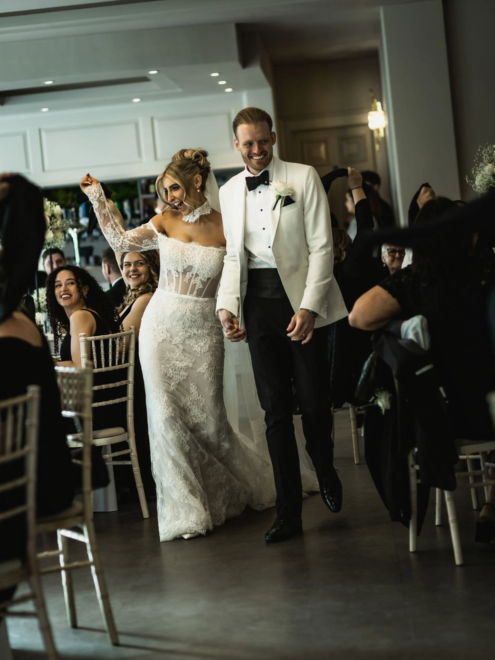 A wedding reception entrance of a groom in white tuxedo and a bride during an Orangery Maidstone wedding in Kent.