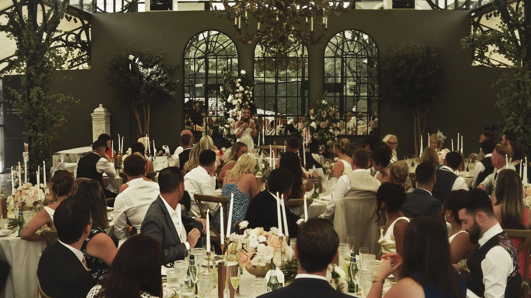 A speaker delivering a toast in the Port Lympne Orangery during the wedding breakfast, framed with editorial composition.