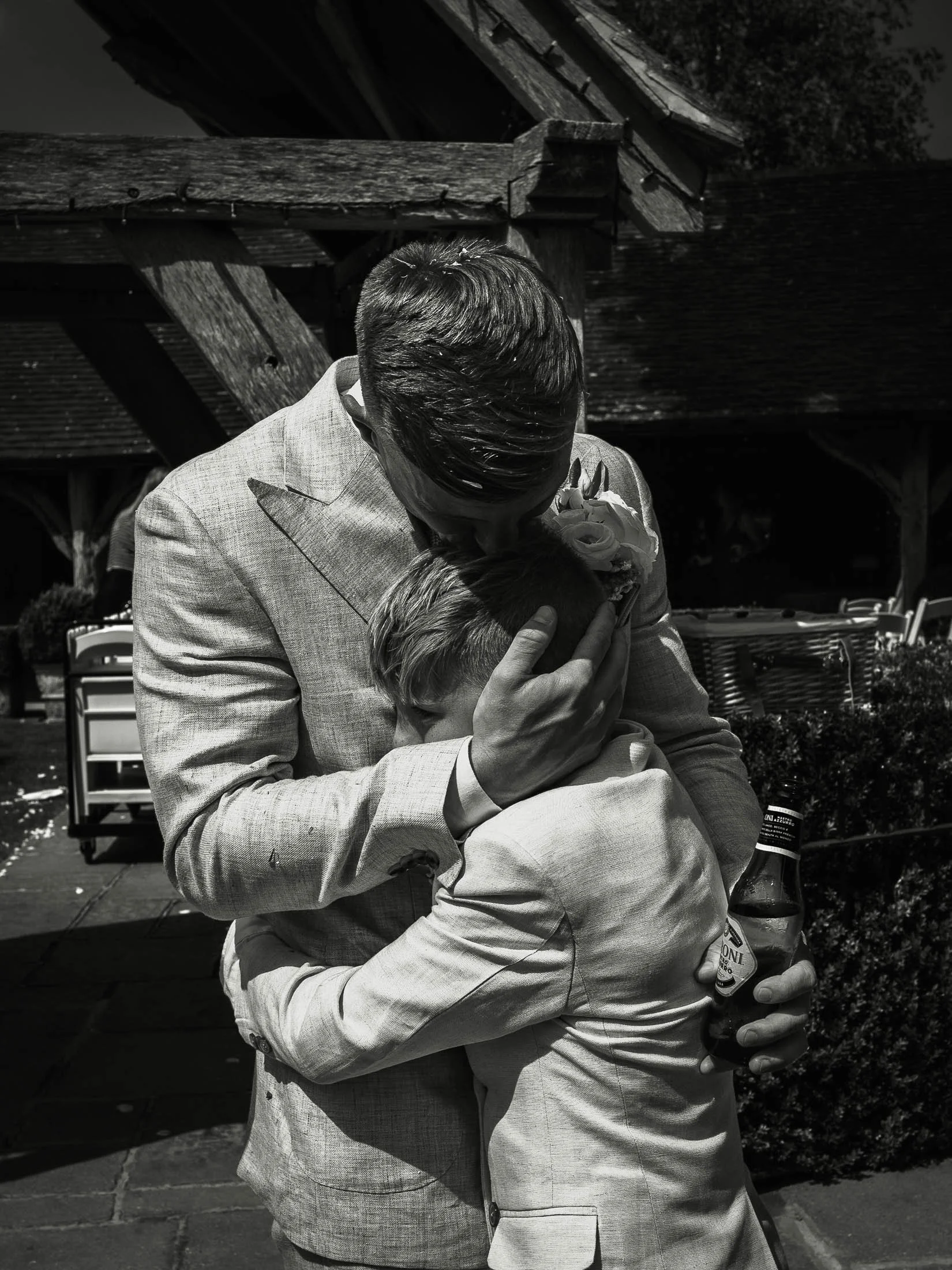 An emotional black and white wedding photograph from Winters Barns, where a groom embraces his son after the outdoor wedding ceremony.
